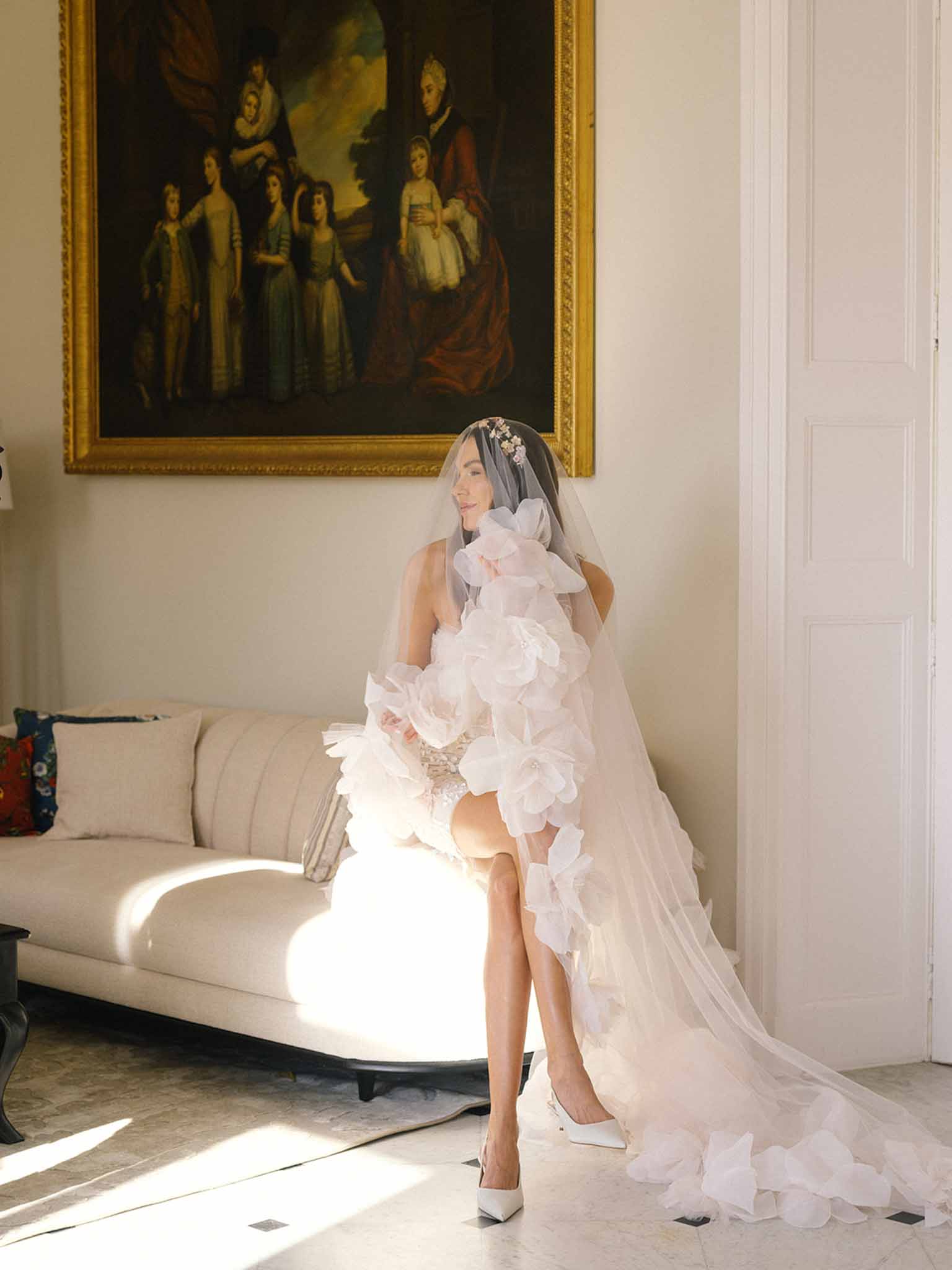 Bride in short white organza dress with veil standing in formal sitting room with classical architecture