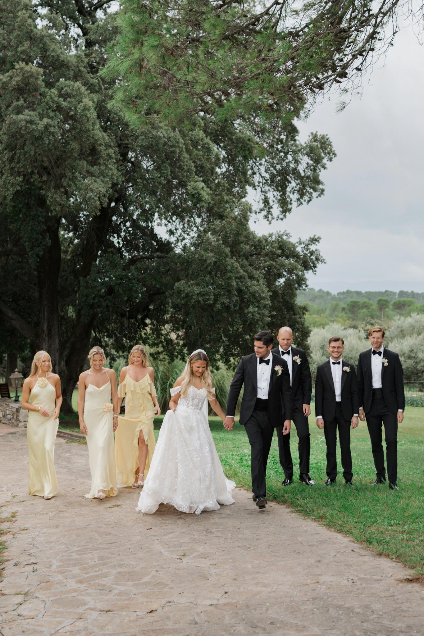 Bride, groom, three groomsmen in tuxedos, and three bridesmaids in butter yellow dresses walking