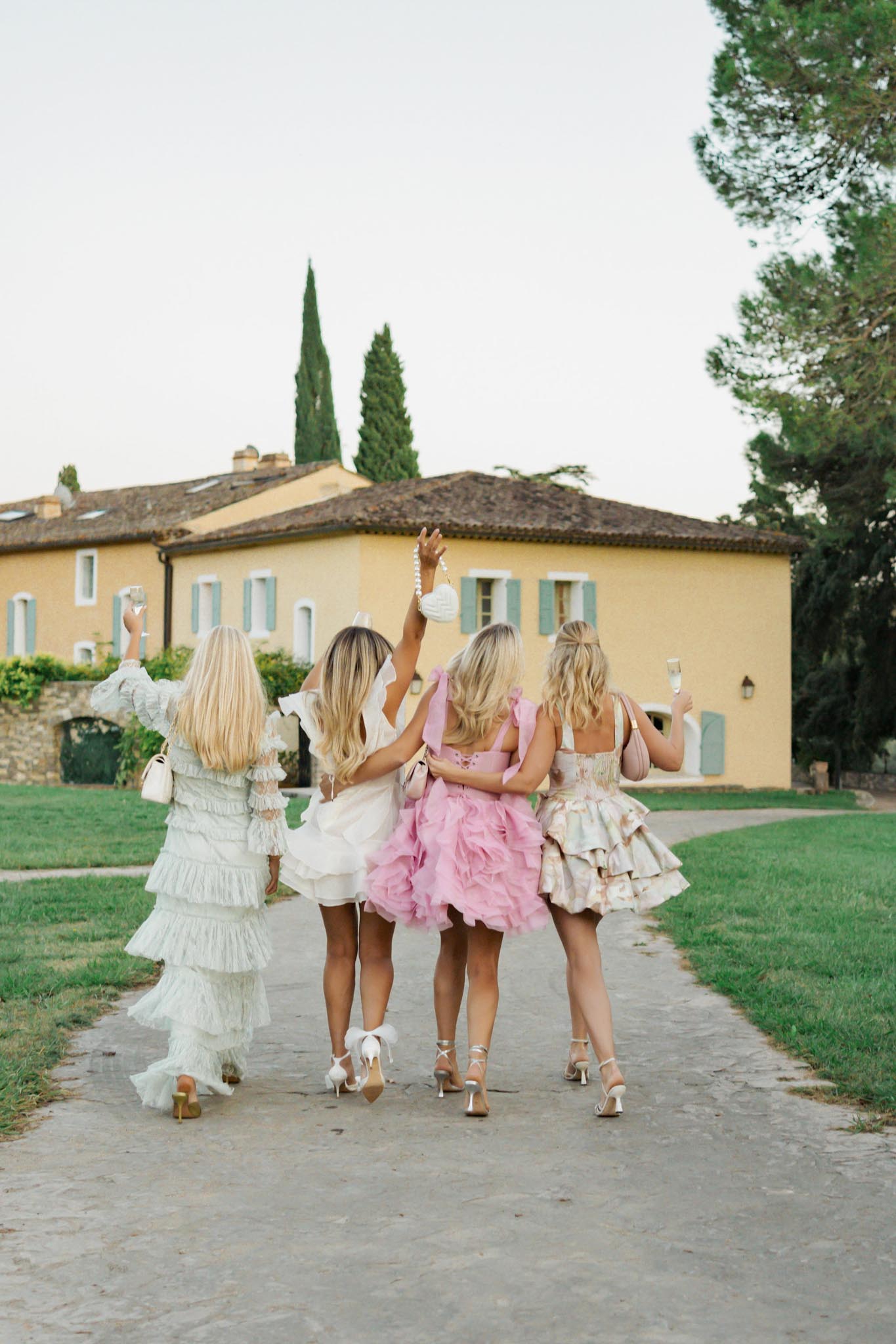 Bridal party walking toward Tuscan villa with champagne flutes raised in celebration