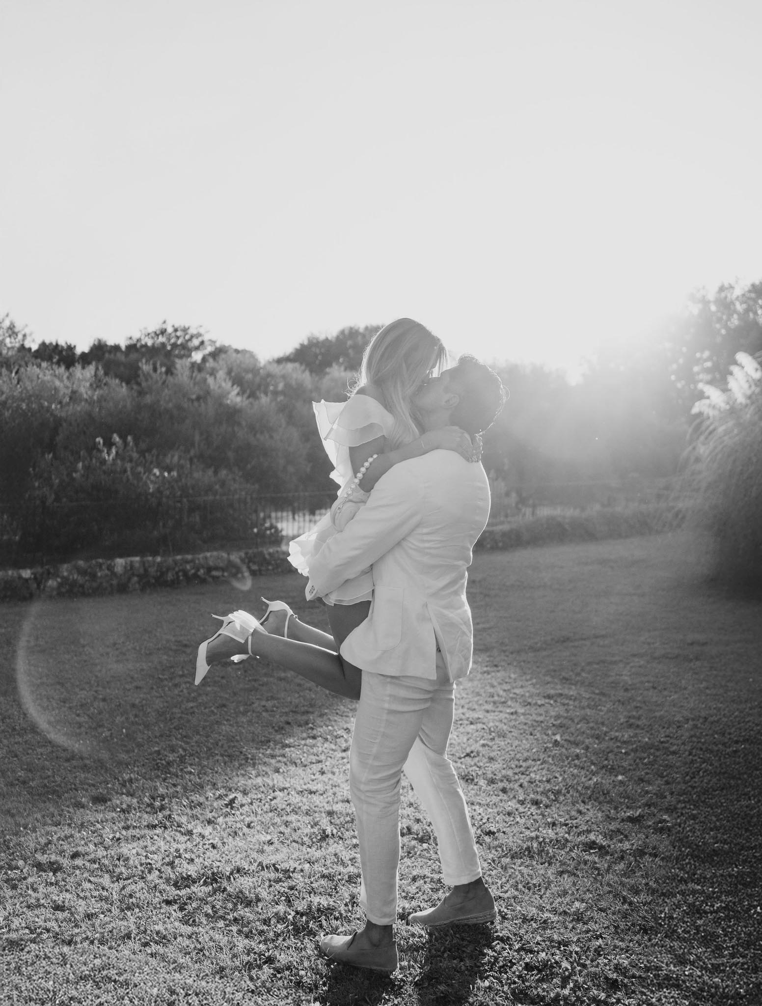 Groom spinning bride in flowing wedding dress on gravel pathway in garden setting