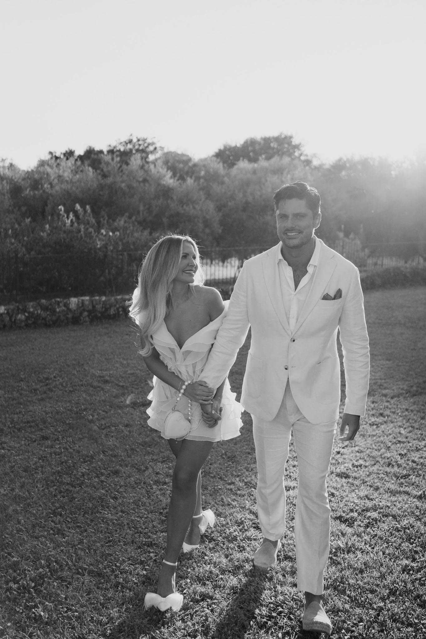 Bride and groom walking hand-in-hand across field in black and white portrait