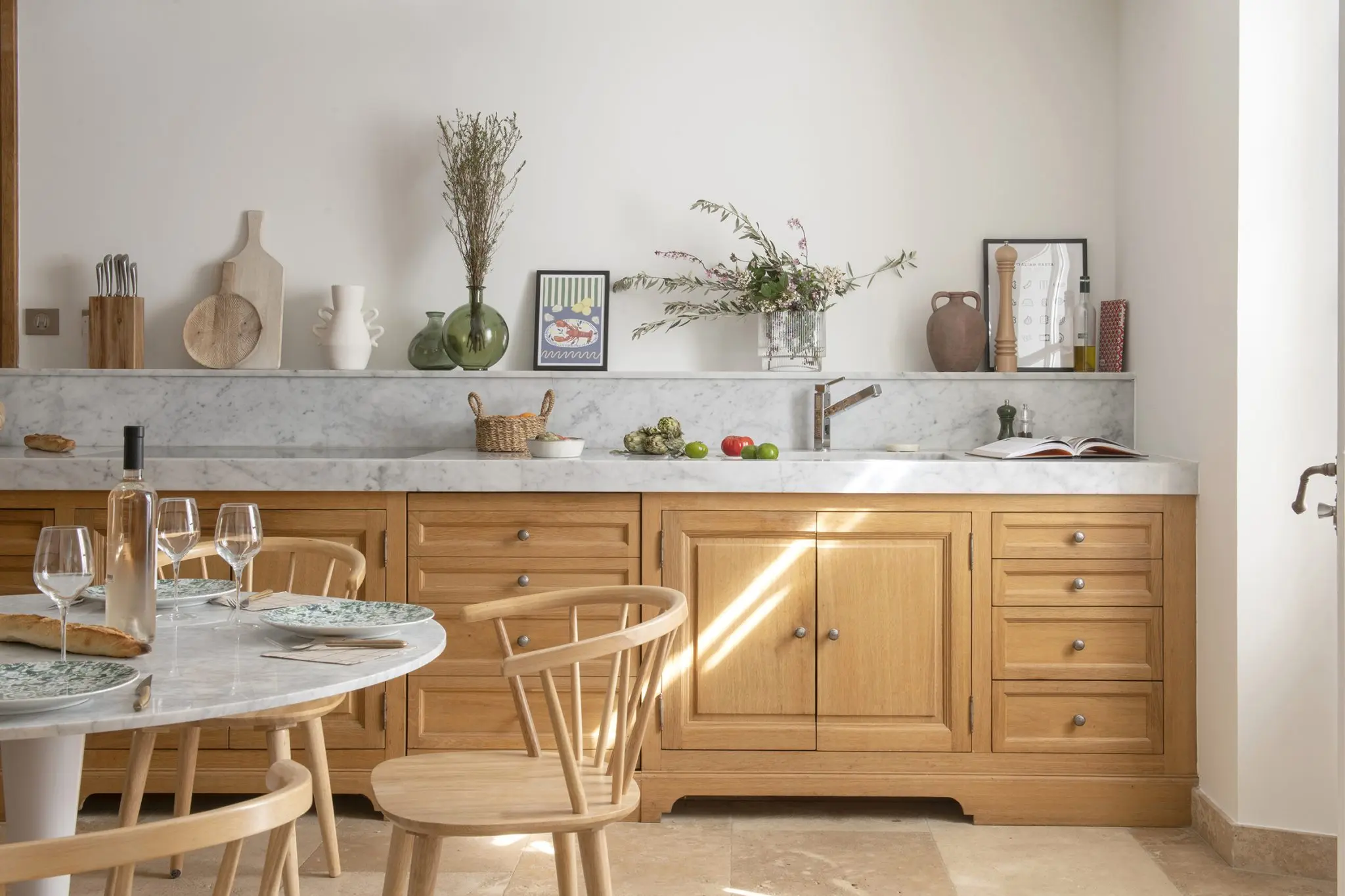 French country-style kitchen with oak cabinetry, marble countertop, round dining table, and ceramic tableware