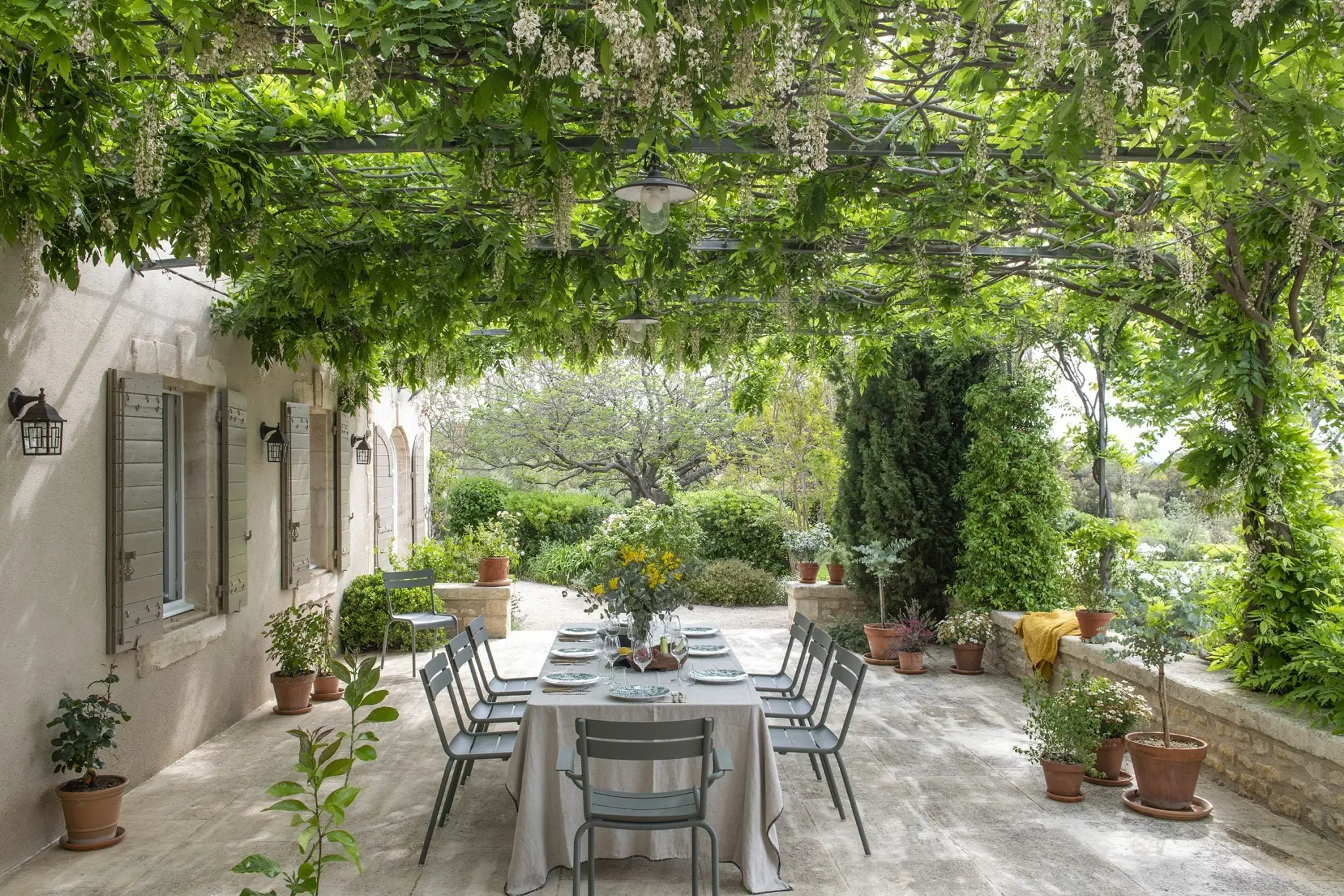 Outdoor terrace dining table under wisteria-covered pergola at Provencal stone property overlooking garden