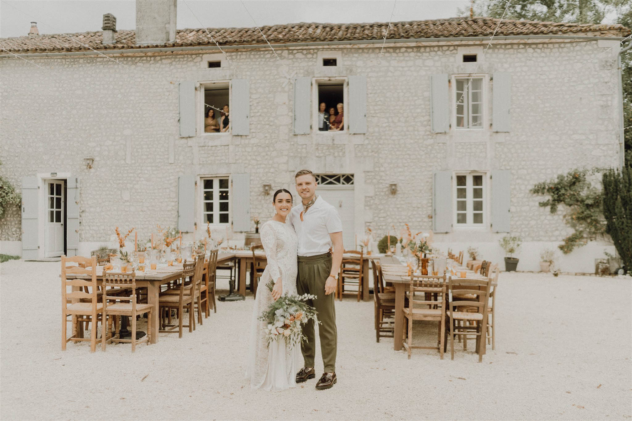 Couple at rustic farm table with amber glassware and terracotta florals before stone farmhouse