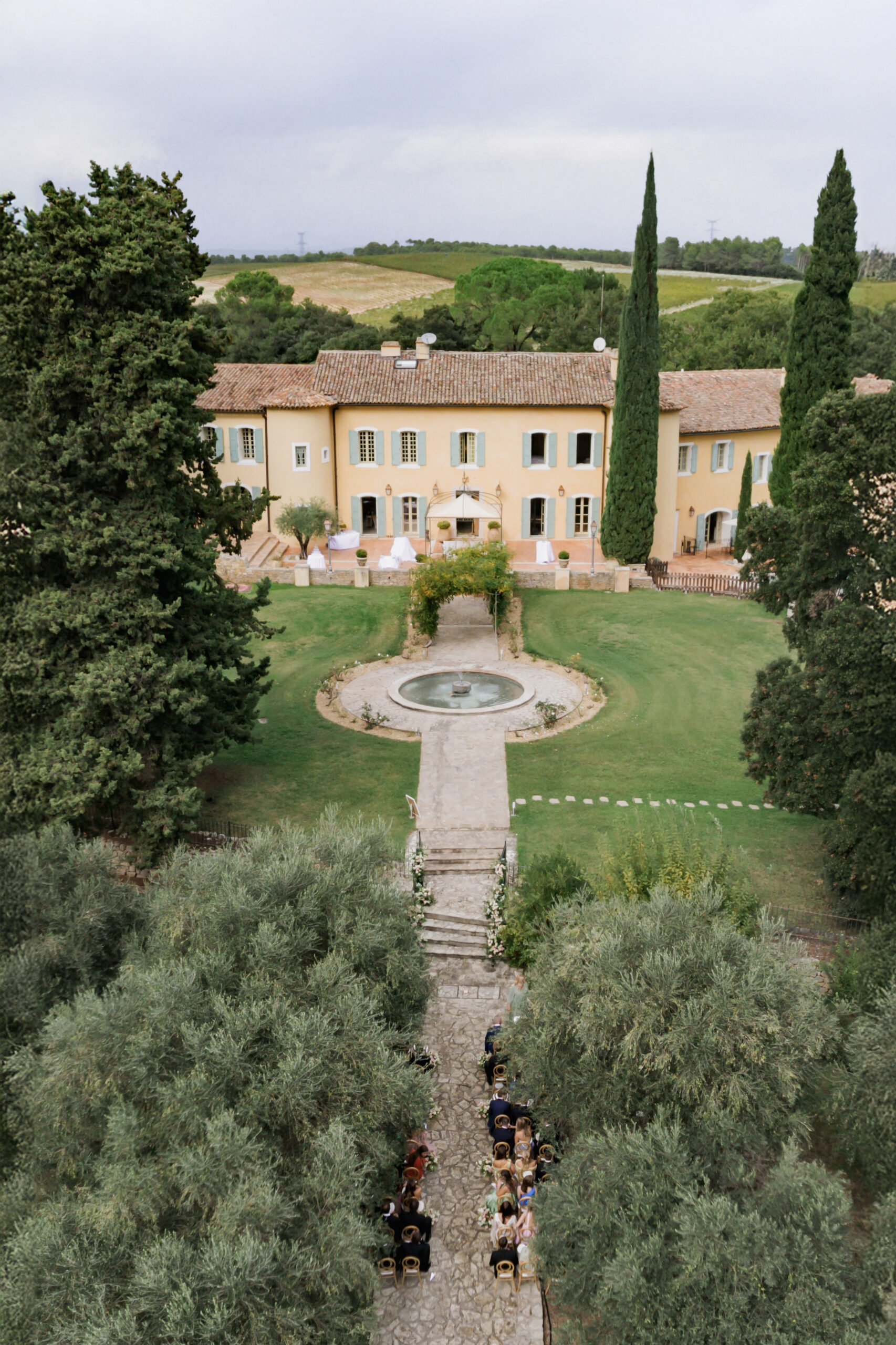 Aerial view of ceremony along olive tree path with gold chairs and Provencal mas behind
