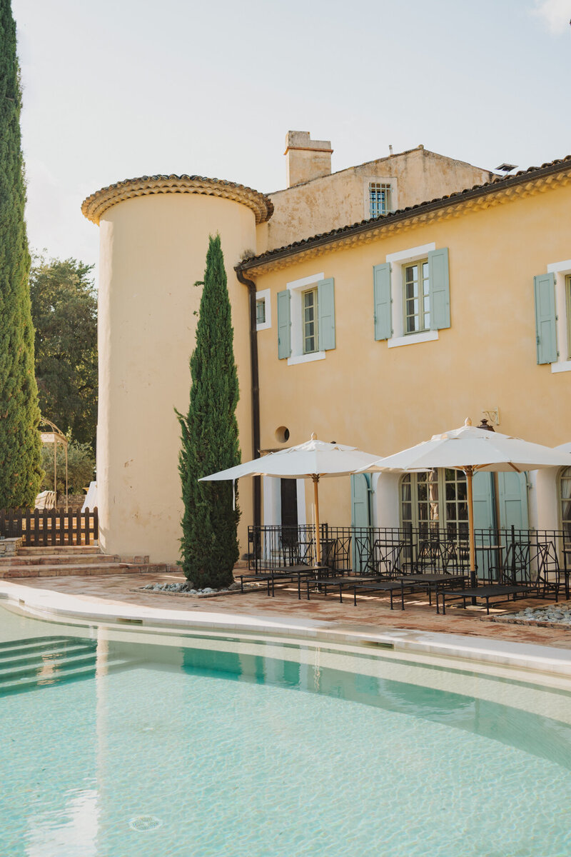 Provencal chateau with ochre walls, blue shutters, pool terrace, and cypress trees