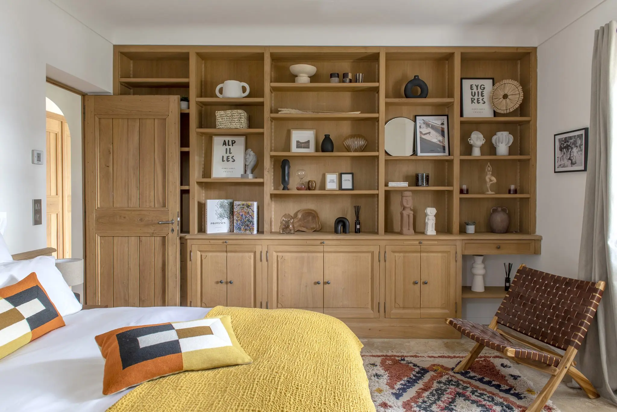 Modern Provencal guest bedroom with oak shelving, mustard coverlet, leather chair, and Berber rug