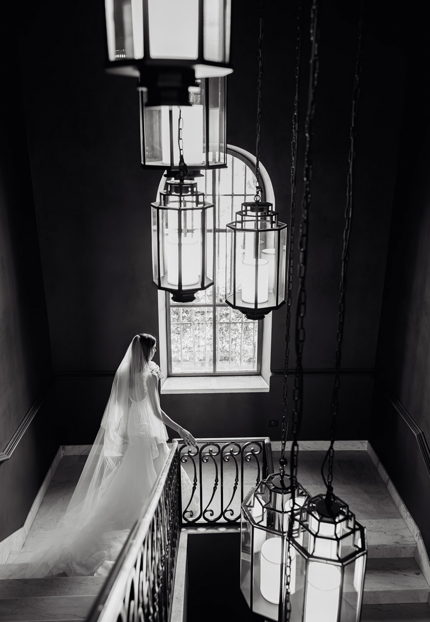 Bride in flowing veil on interior stairwell with wrought-iron railing and architectural lighting