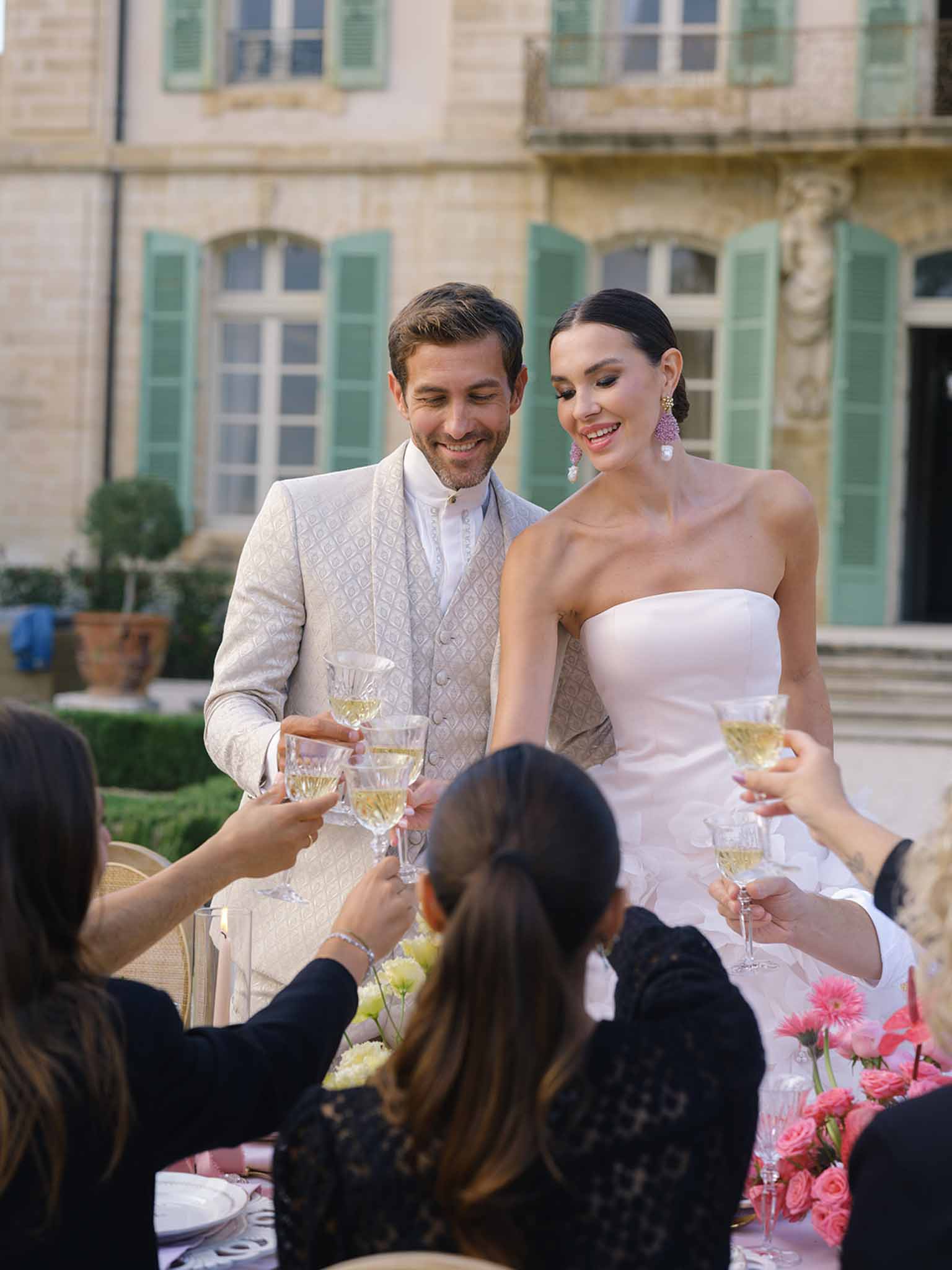 Bride and groom toasting with guests during reception in classical stone courtyard with arched windows