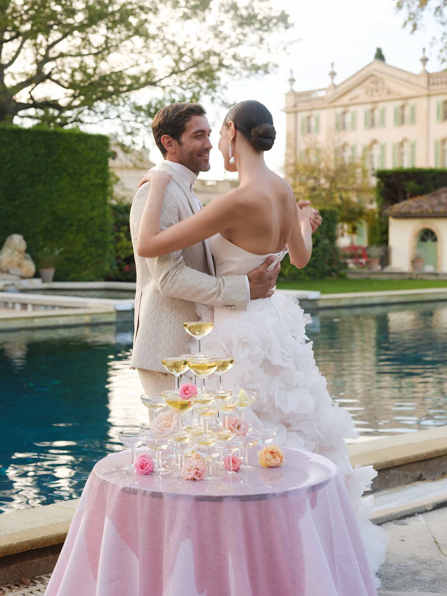 Bride and groom dancing poolside at elegant European estate reception with champagne tower
