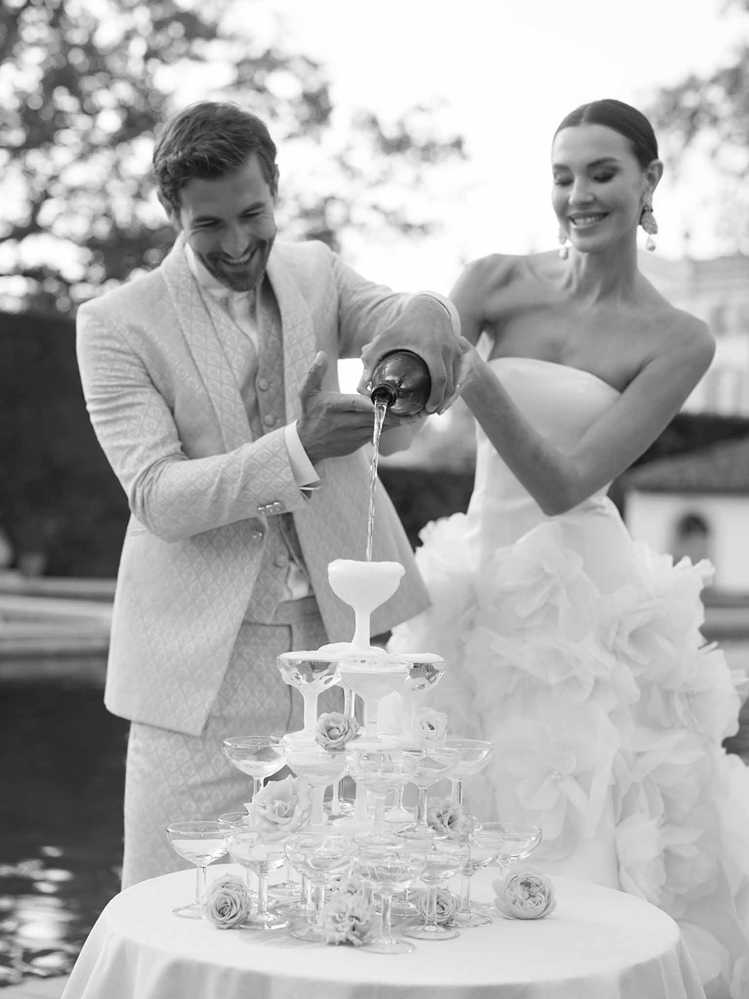 Bride and groom pouring champagne tower during wedding reception at garden venue