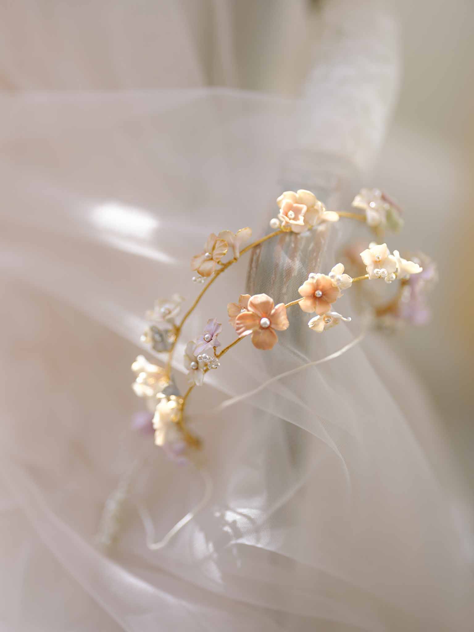 Close-up of bridal hair accessory with ceramic flowers and pearl centers against ivory tulle backdrop