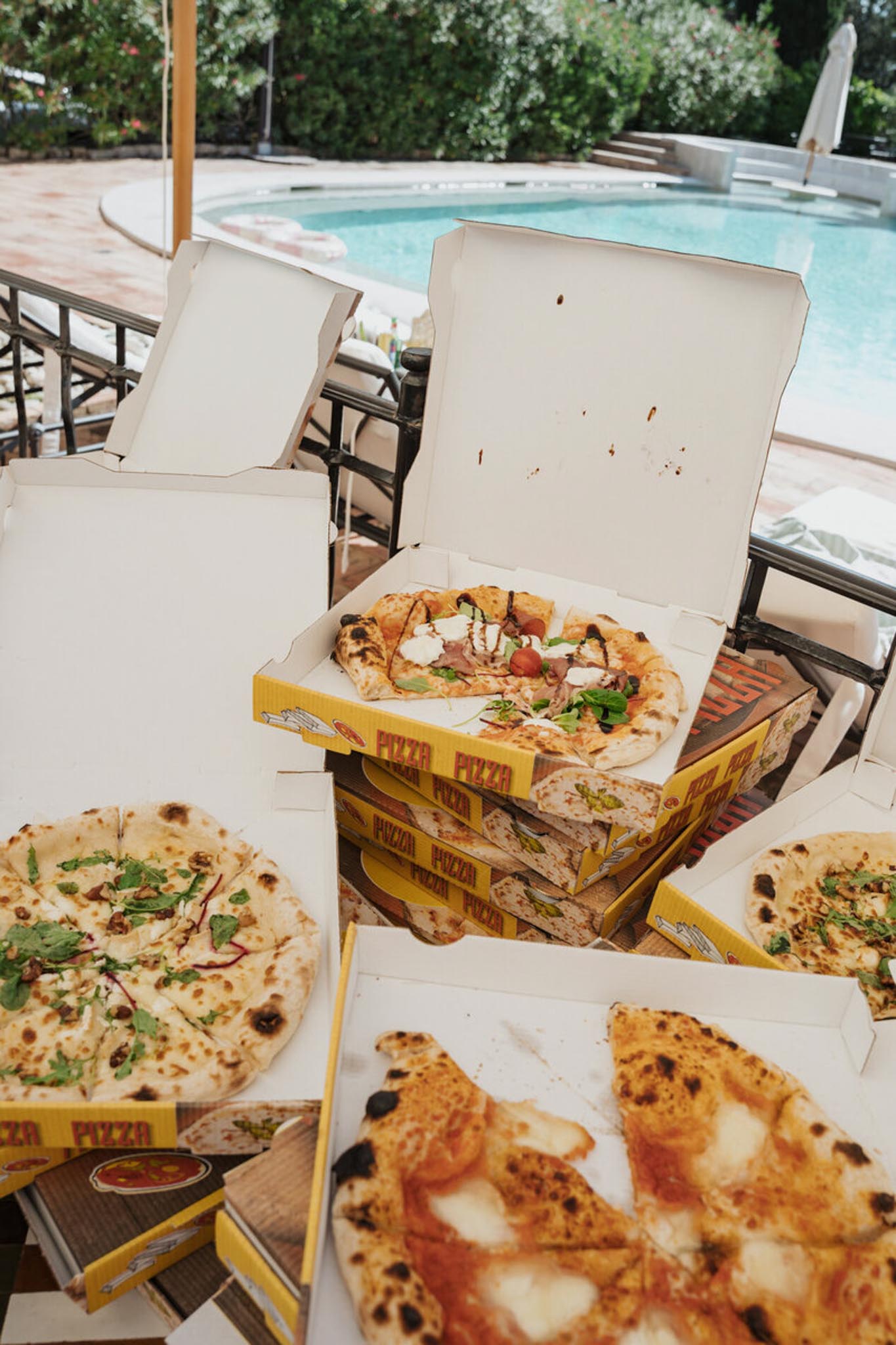 Neapolitan pizzas in yellow boxes spread across poolside sun loungers at late-night reception