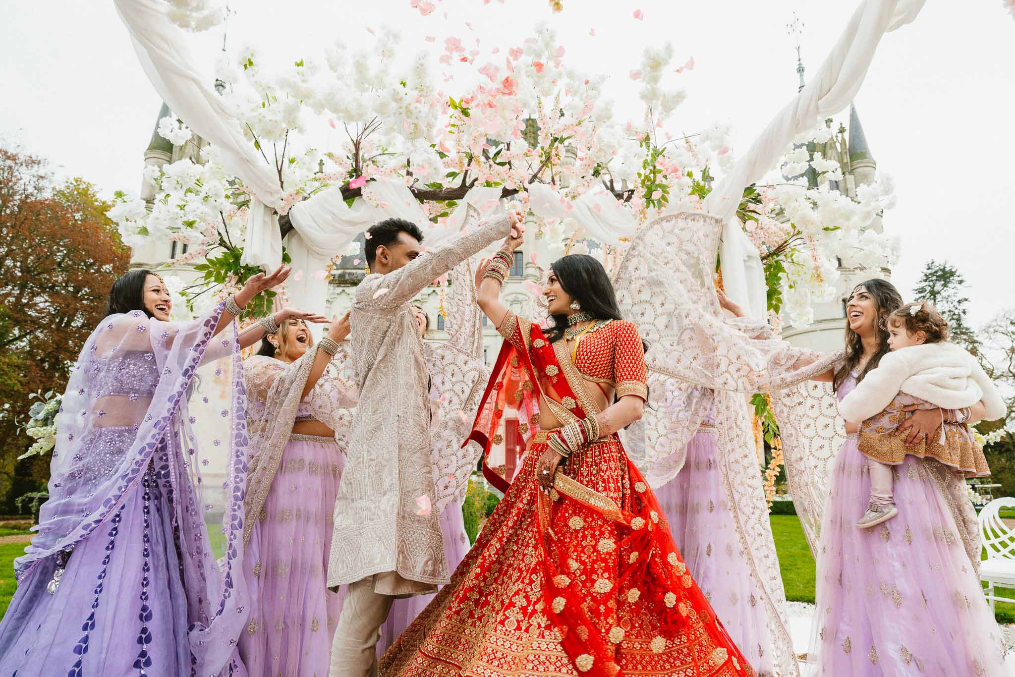 Bride and groom celebrating post-ceremony moment with flower petals under floral canopy in outdoor garden setting