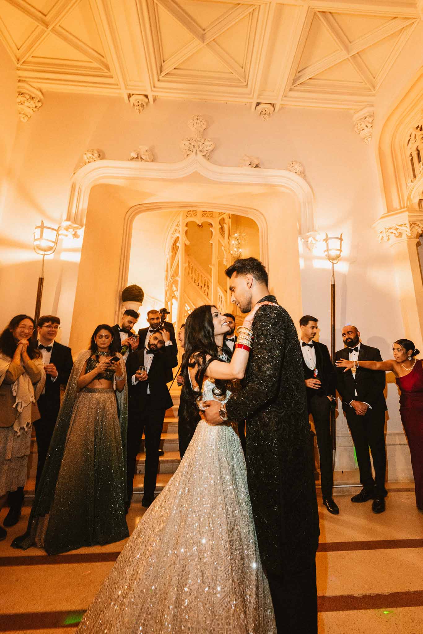 Couple's first dance in ornate classical ballroom with guests watching in formal attire