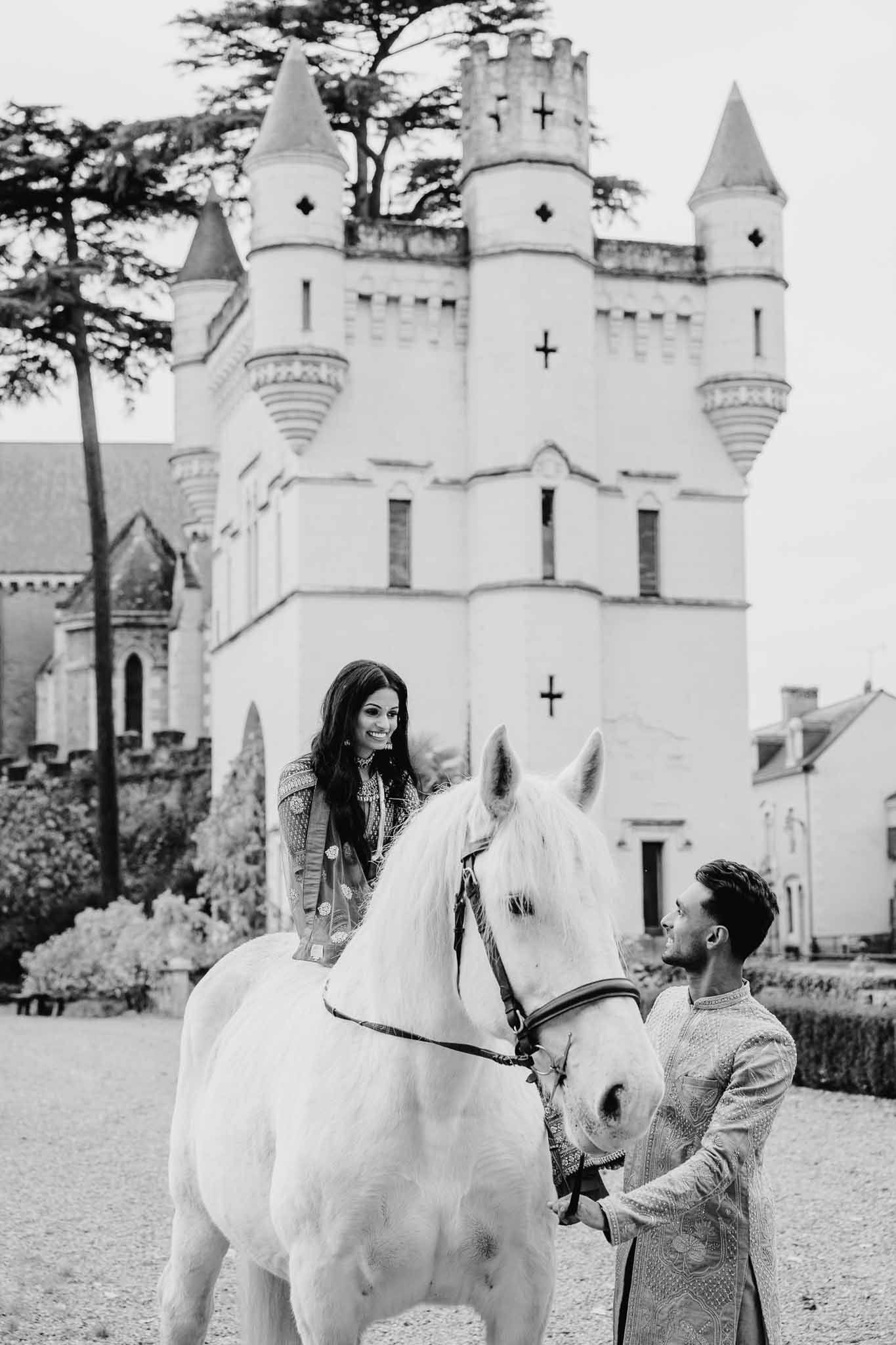 Bride and groom with white horse in front of castle with turrets and battlements