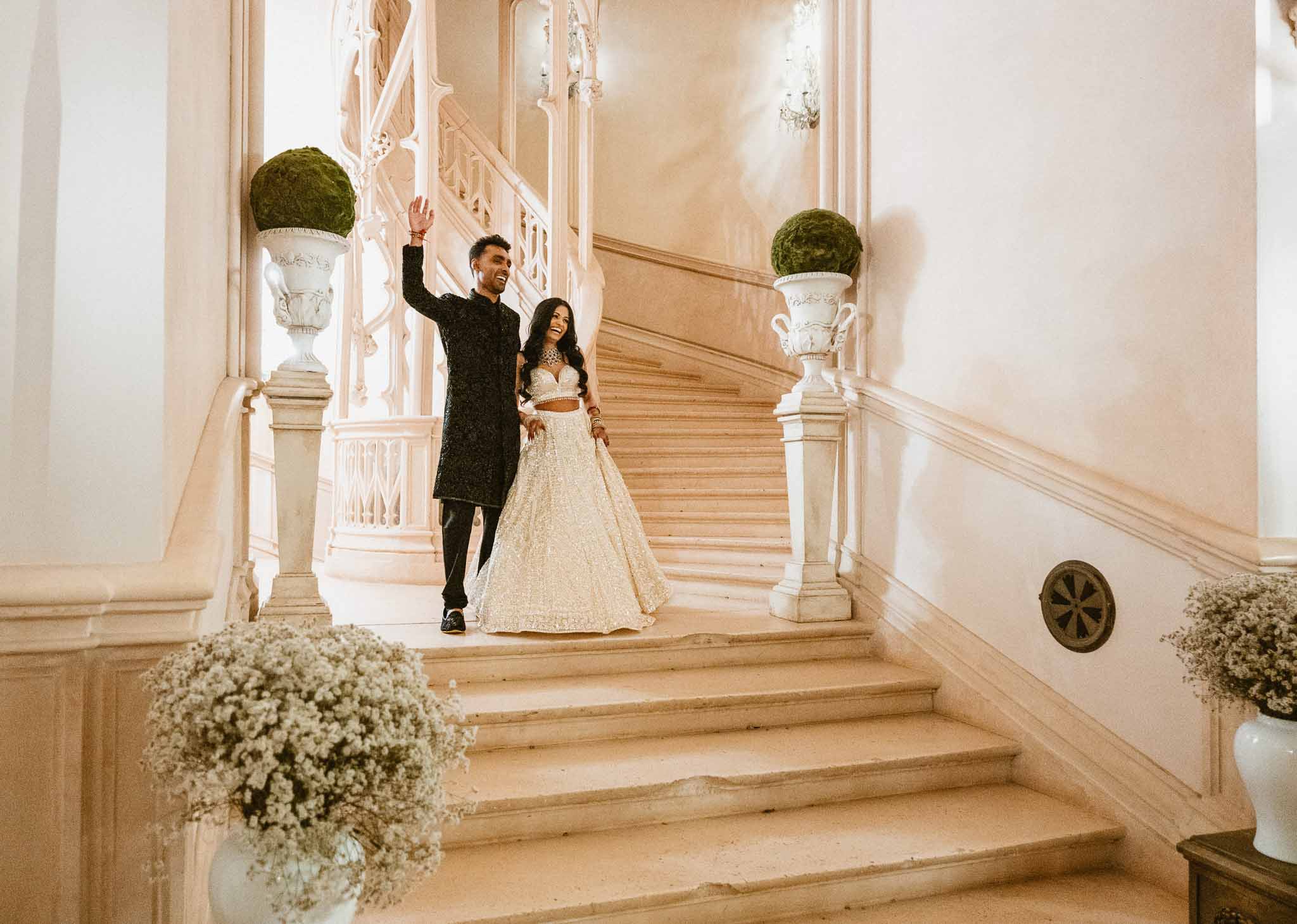 Bride and groom celebrating on grand wooden staircase in classical interior venue