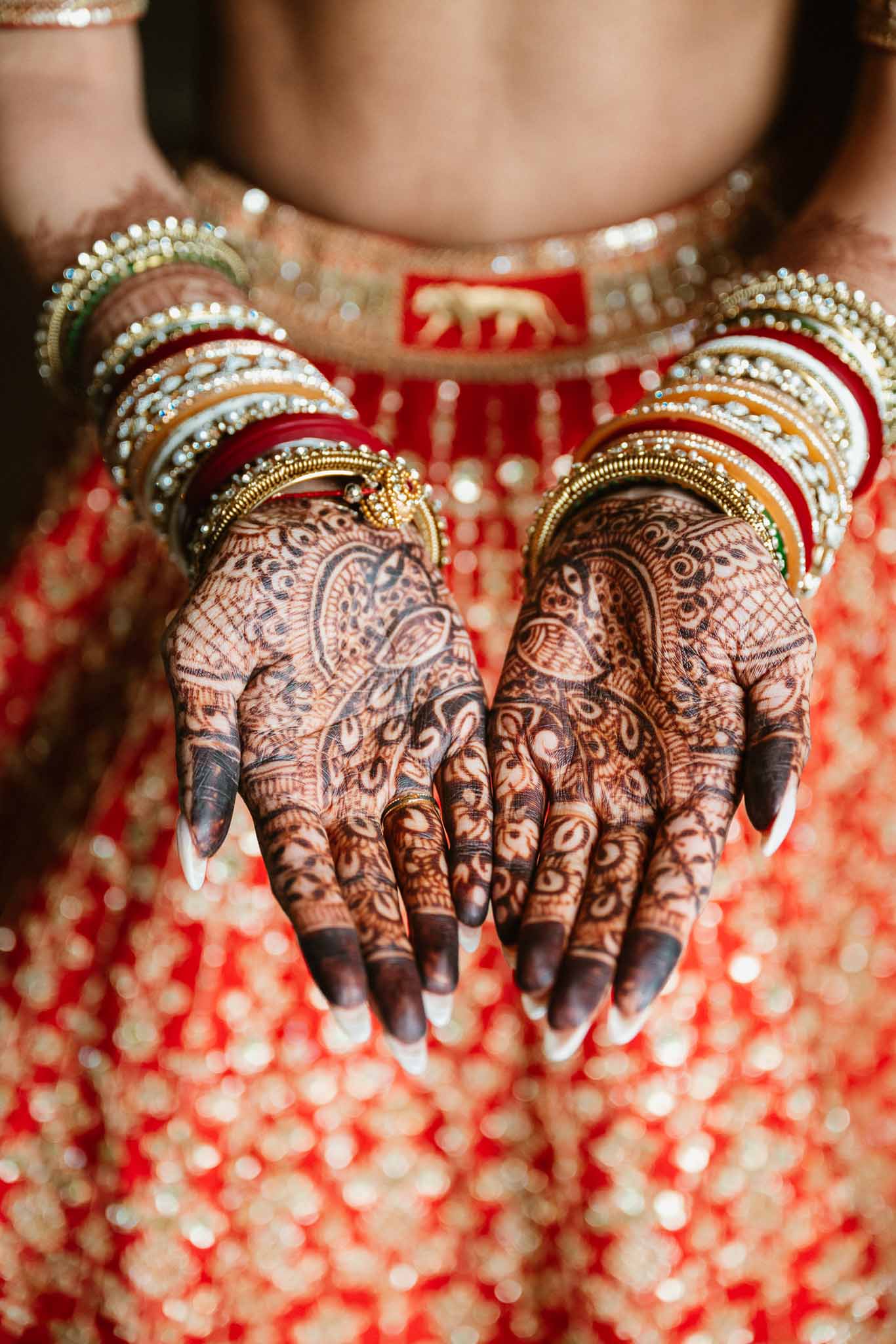 Bride's hands with intricate mehendi henna patterns and traditional gold bangles at South Asian wedding