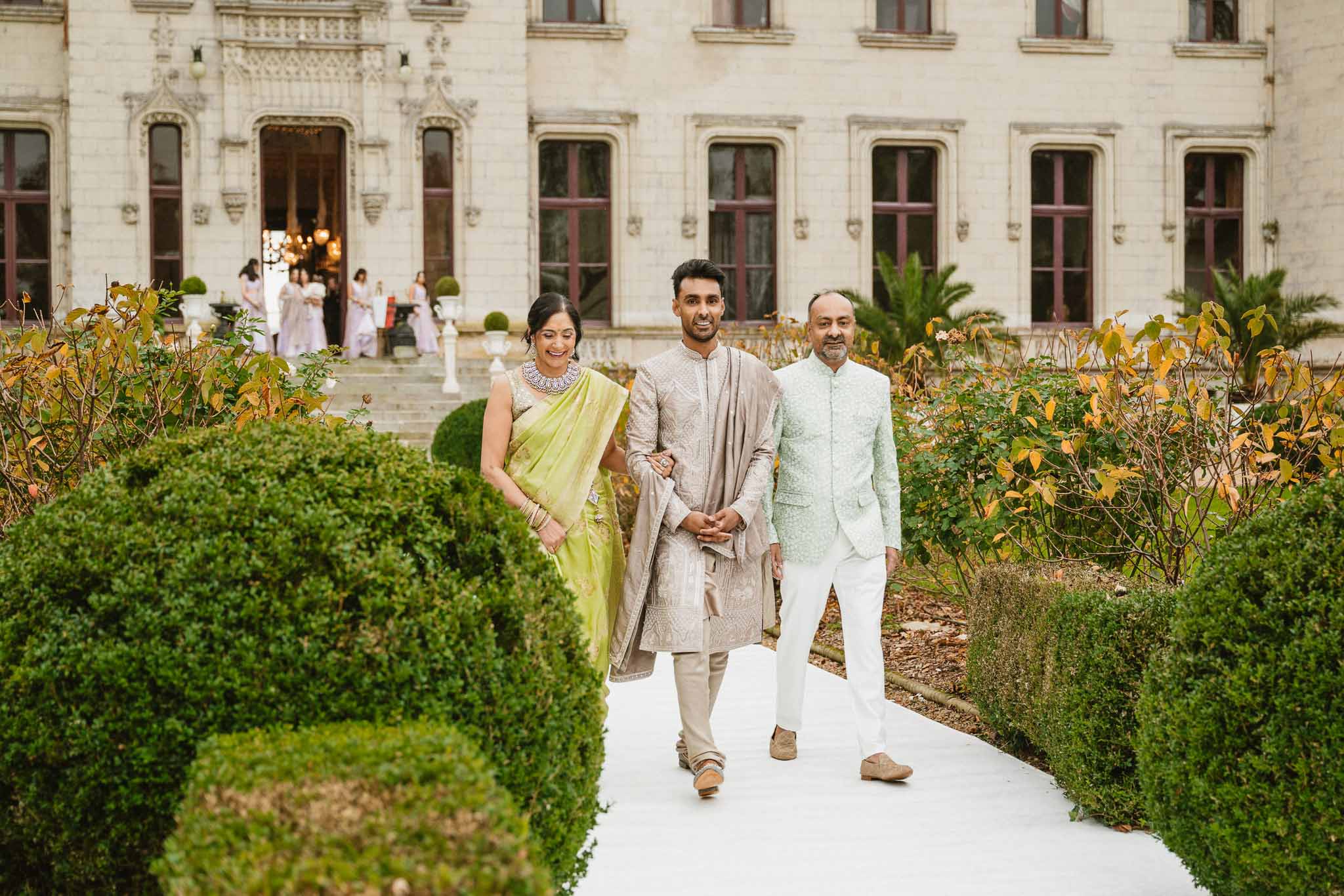 Bride and groom with family member walking through formal garden courtyard at European palazzo