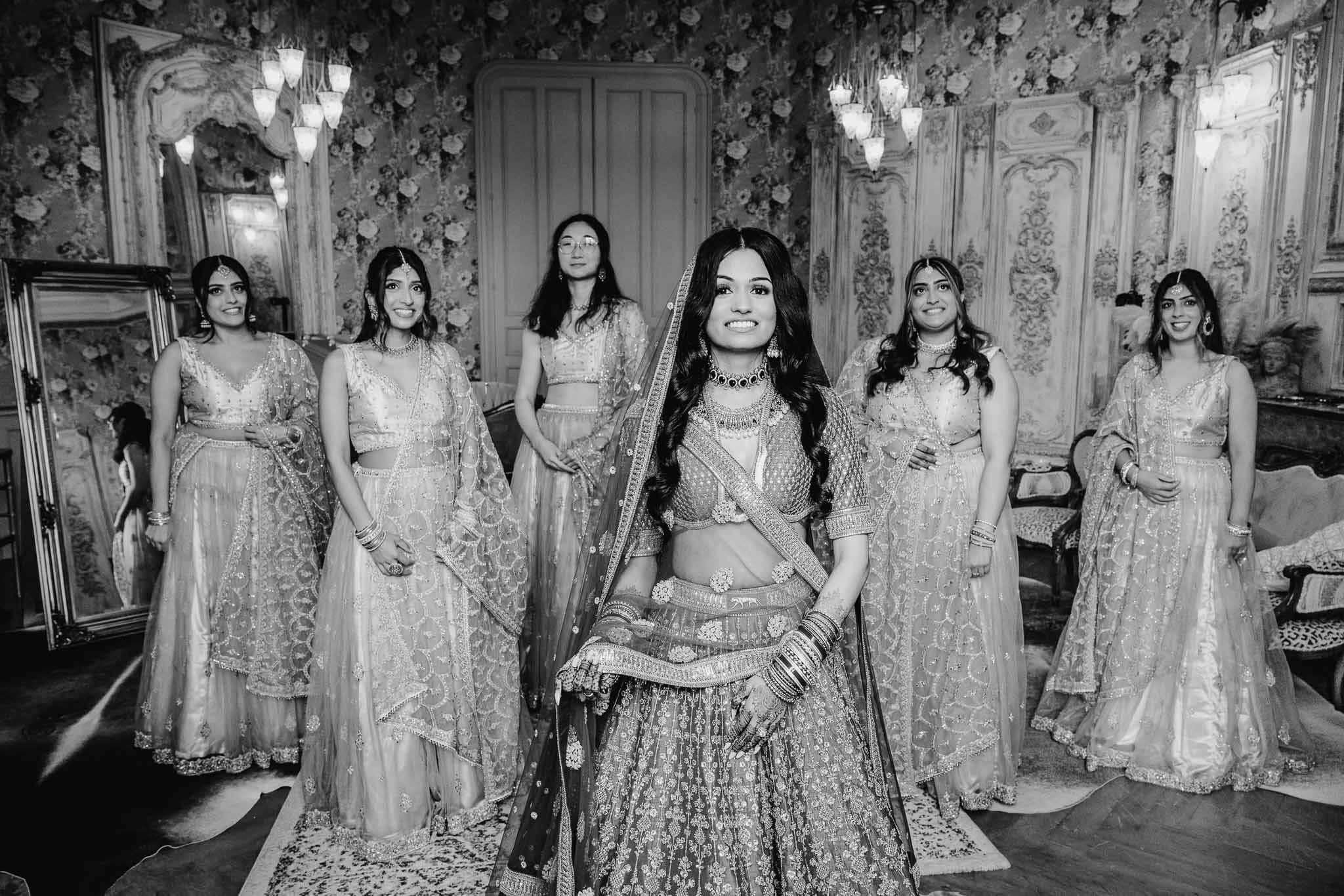 Bride in traditional lehenga with bridesmaids during preparation in ornate indoor venue