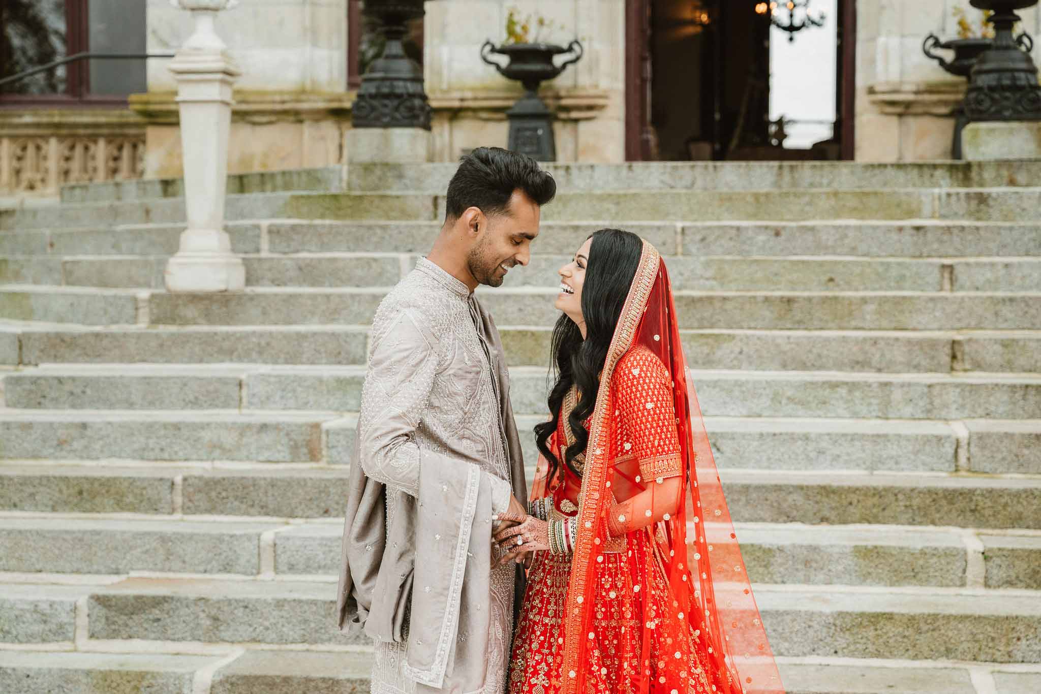 Bride and groom in traditional attire pose on stone staircase at classical European venue