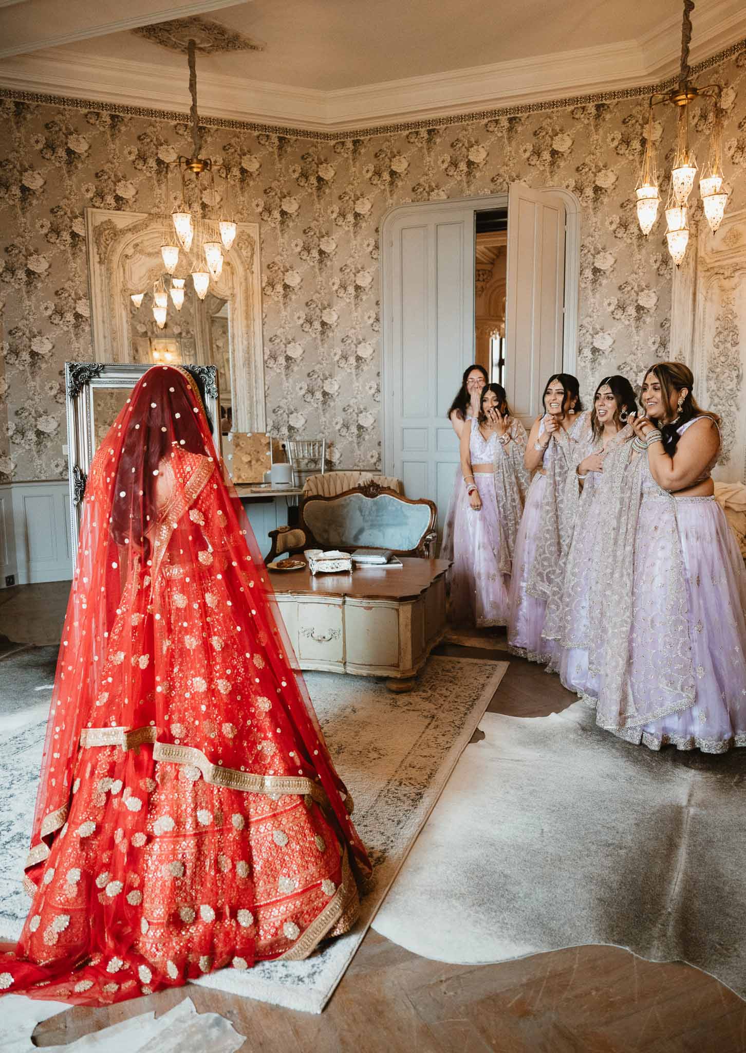 Bride in red lehenga with bridesmaids in lavender during getting ready in luxurious dressing room