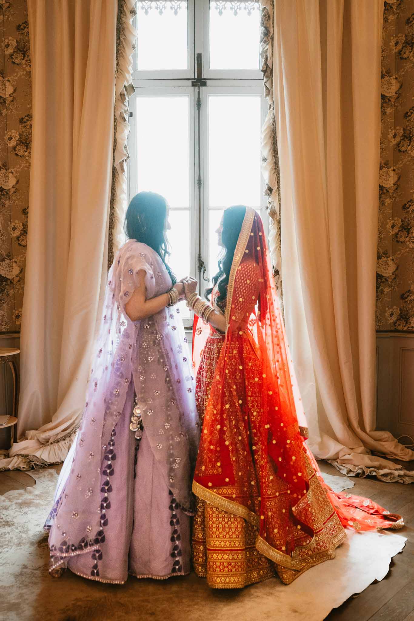 Two women in traditional South Asian bridal attire during wedding preparation in elegant indoor room