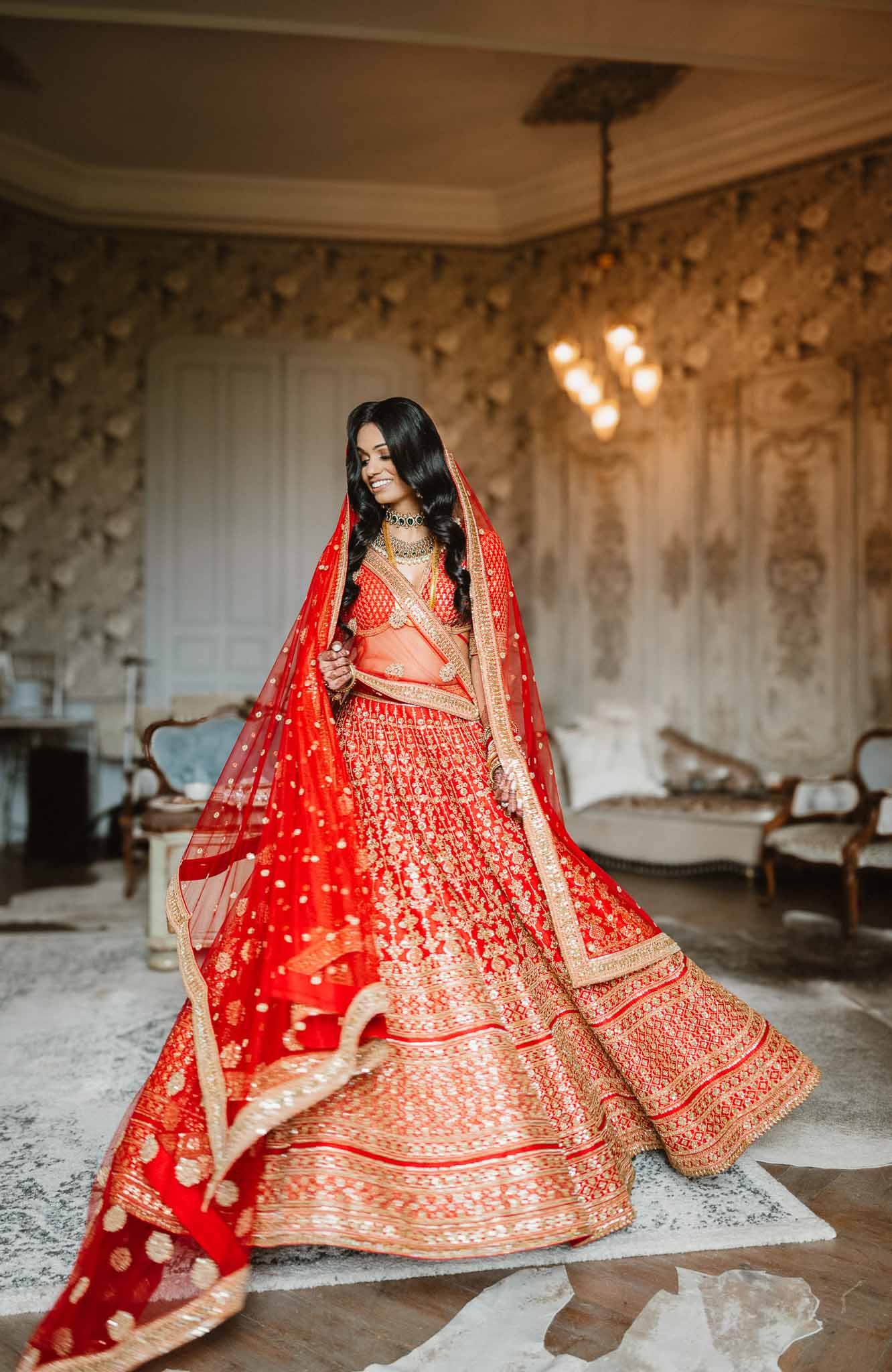 Bride in traditional red and gold Indian lehenga in classical interior room