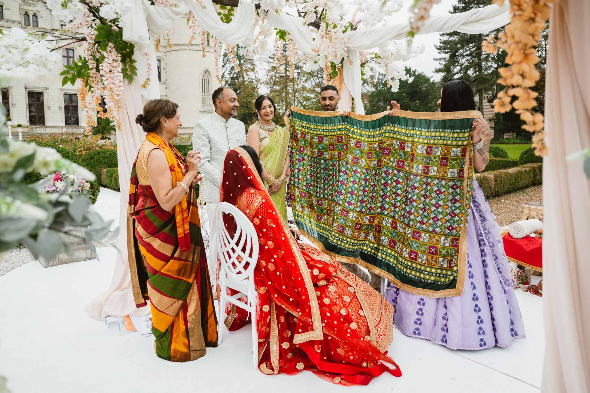 Bride and groom displaying traditional textiles with family at outdoor courtyard wedding celebration