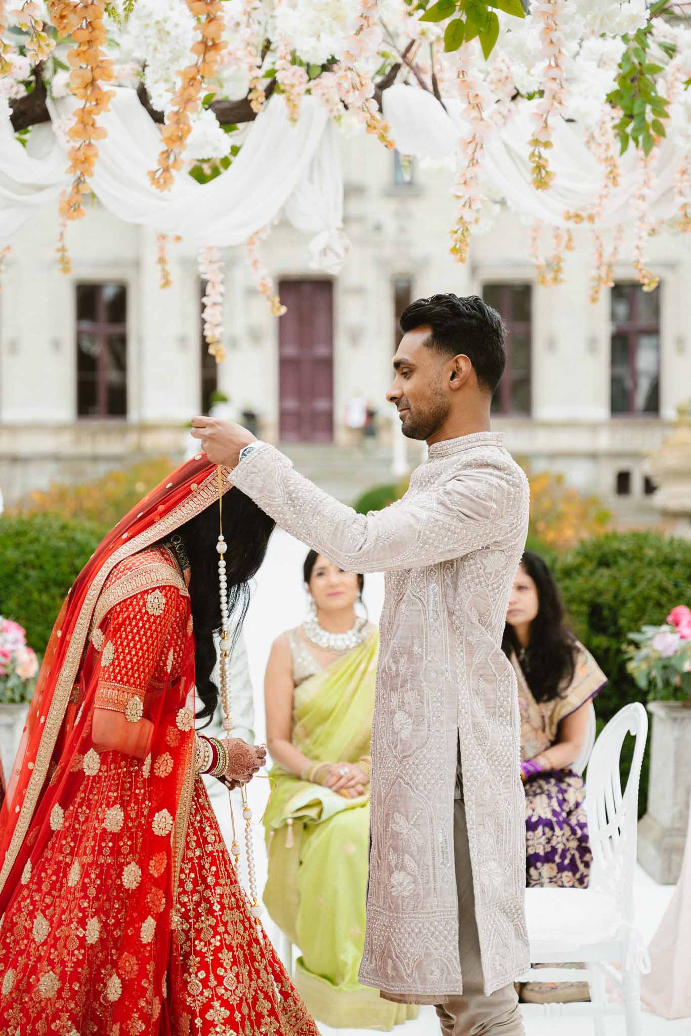 Groom adjusting bride's veil during South Asian wedding ceremony in classical courtyard setting