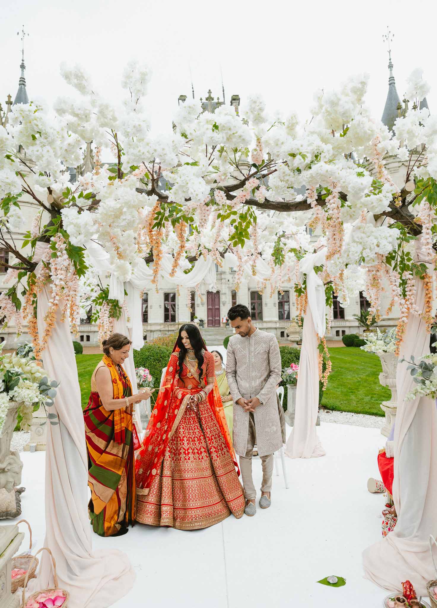 Indian wedding couple walking through floral archway during ceremony at classical white manor house