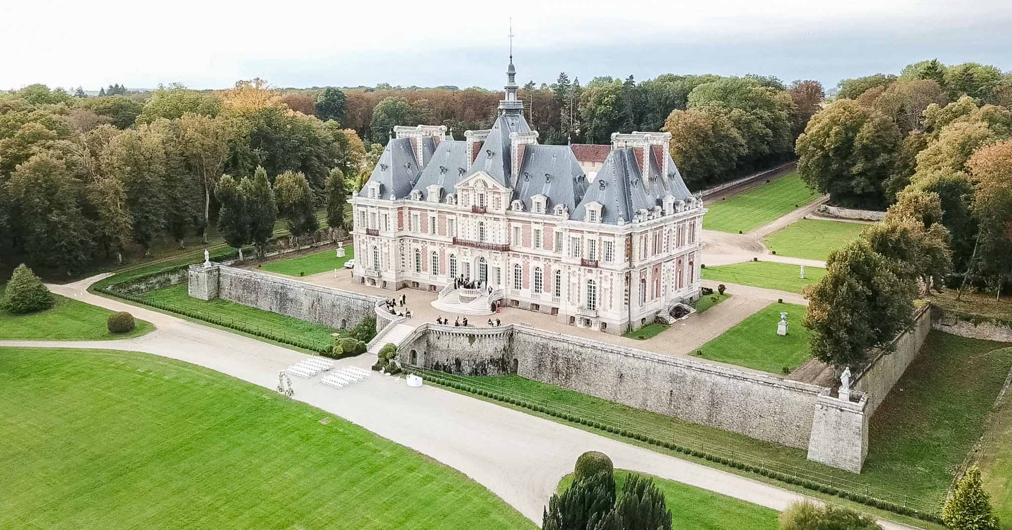 Aerial view of pink Renaissance château with formal gardens and wedding ceremony setup on terrace