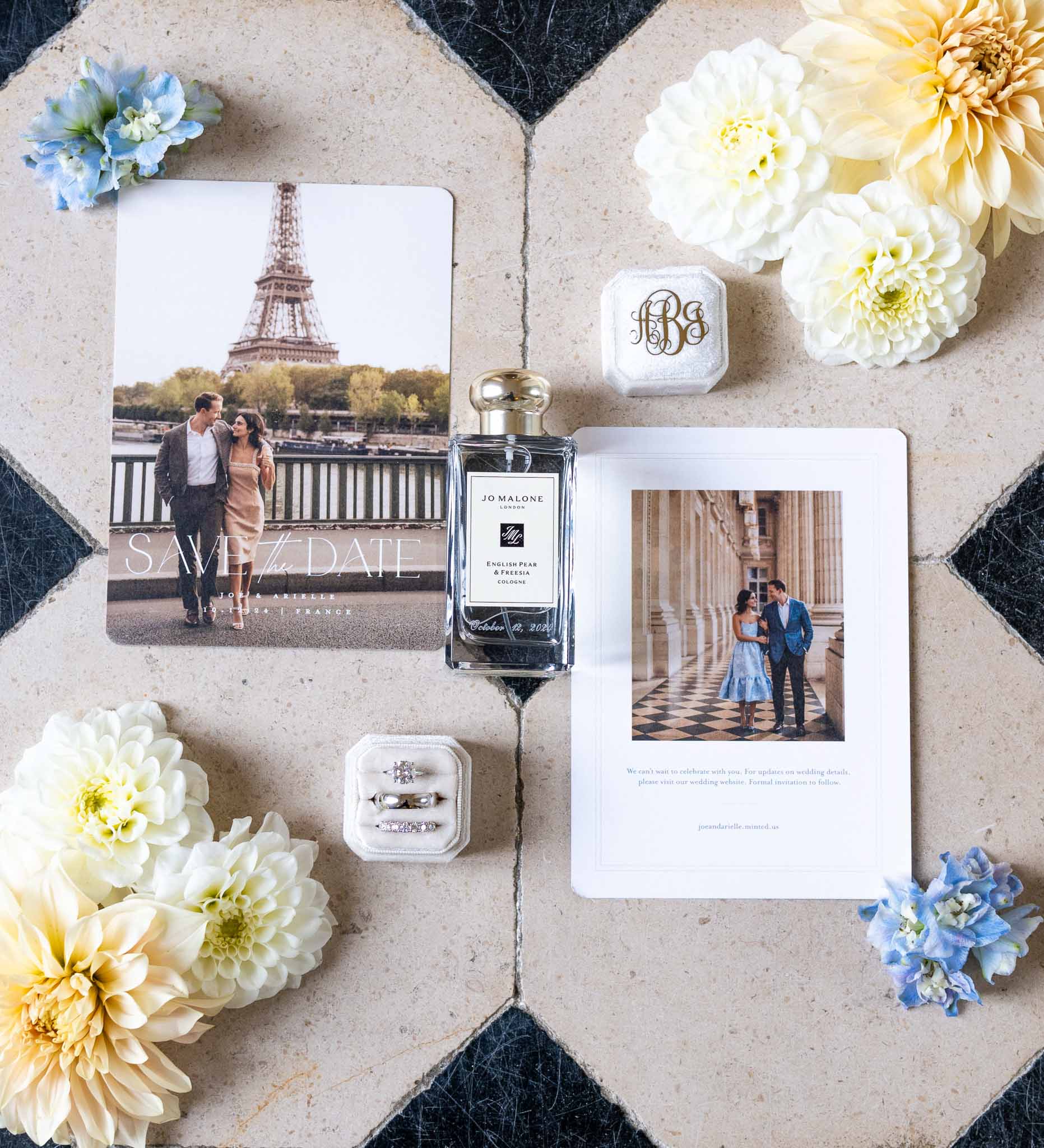 Wedding invitation suite flat lay with rings, perfume, and white dahlias on geometric stone surface
