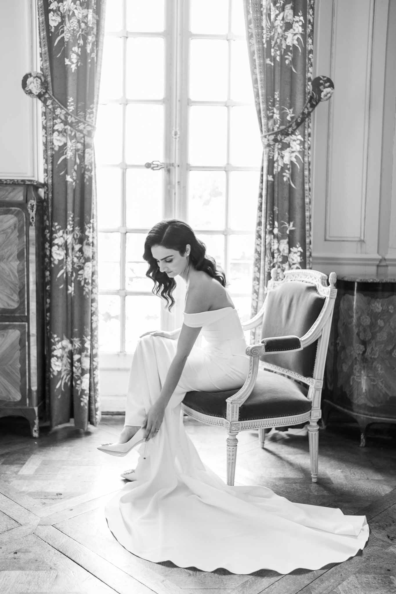 Bride in minimalist gown seated in Louis XVI chair during getting ready moment in elegant period room