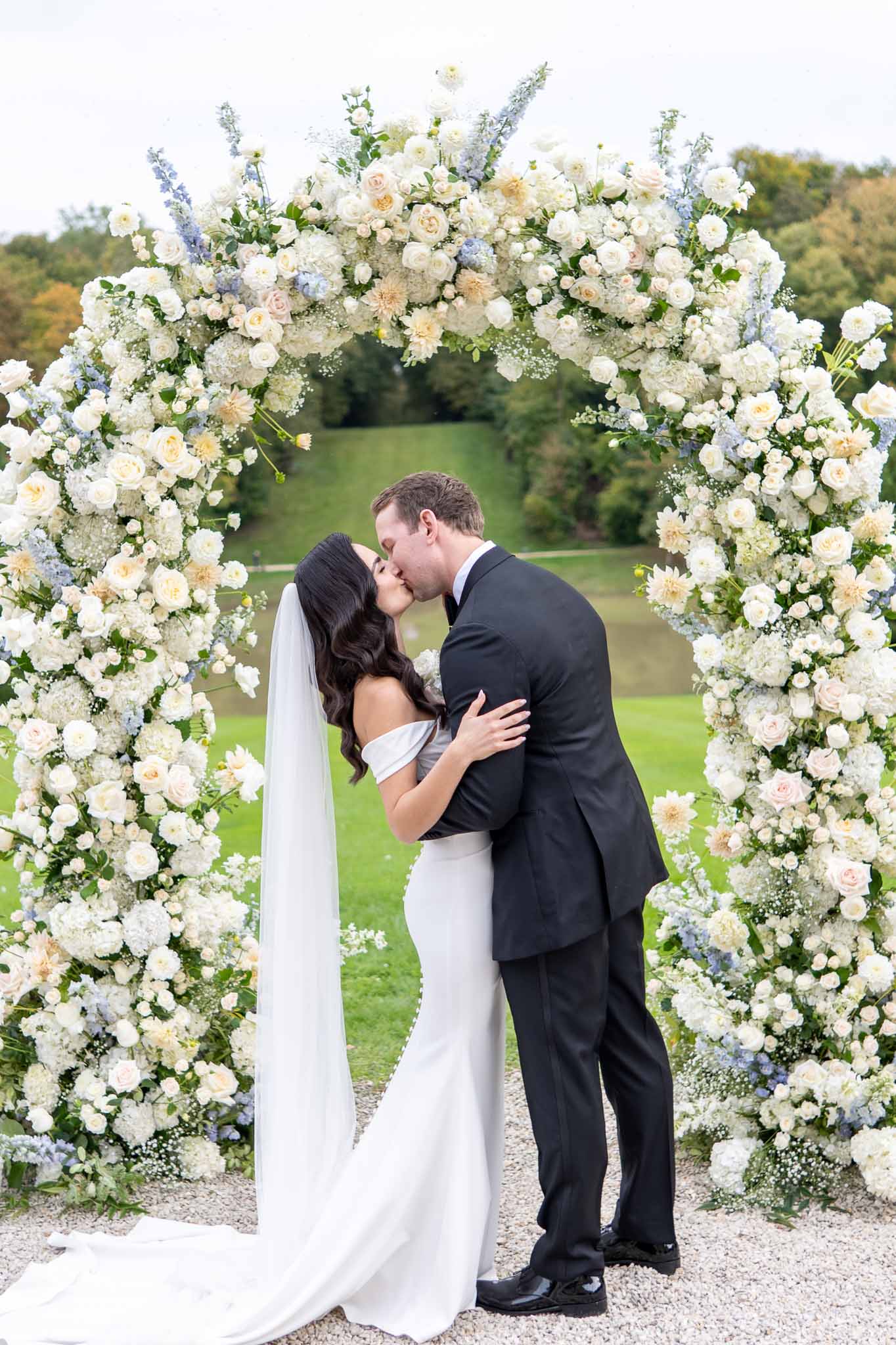 Bride and groom first kiss under floral arch during outdoor garden ceremony