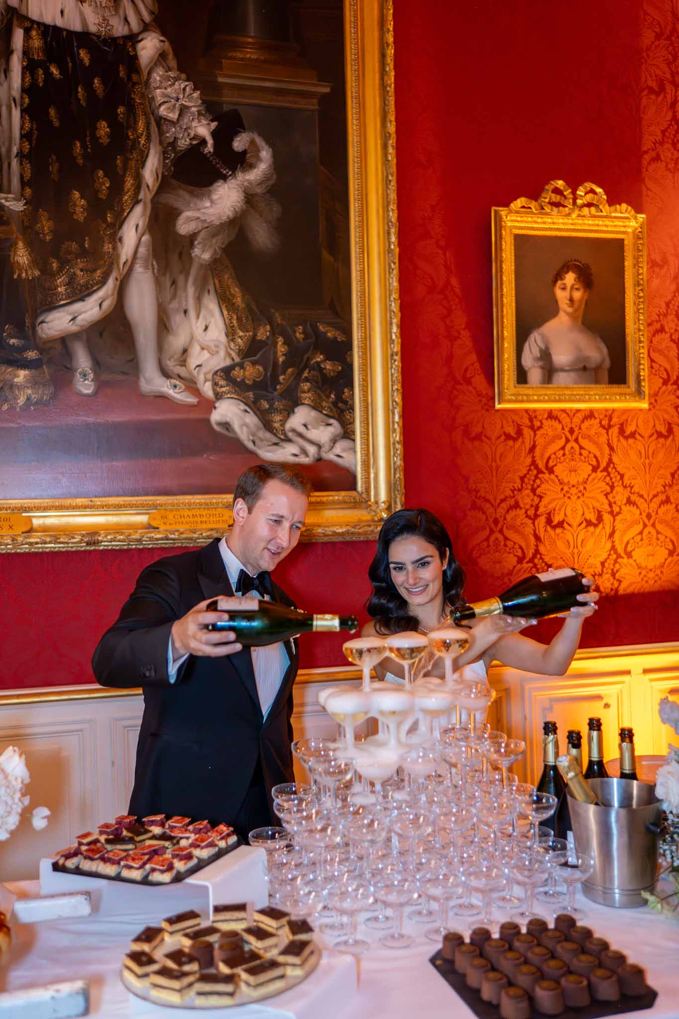 Bride and groom with champagne at elegant château cocktail reception with red damask walls