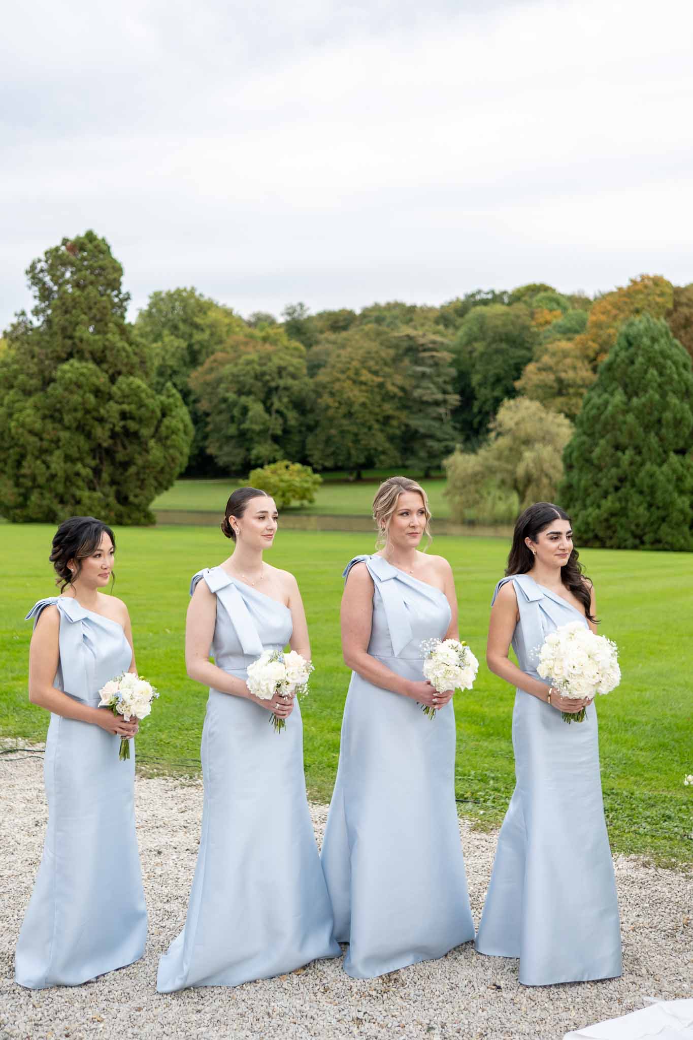 Four bridesmaids in pale blue gowns holding white hydrangea bouquets at estate grounds wedding venue