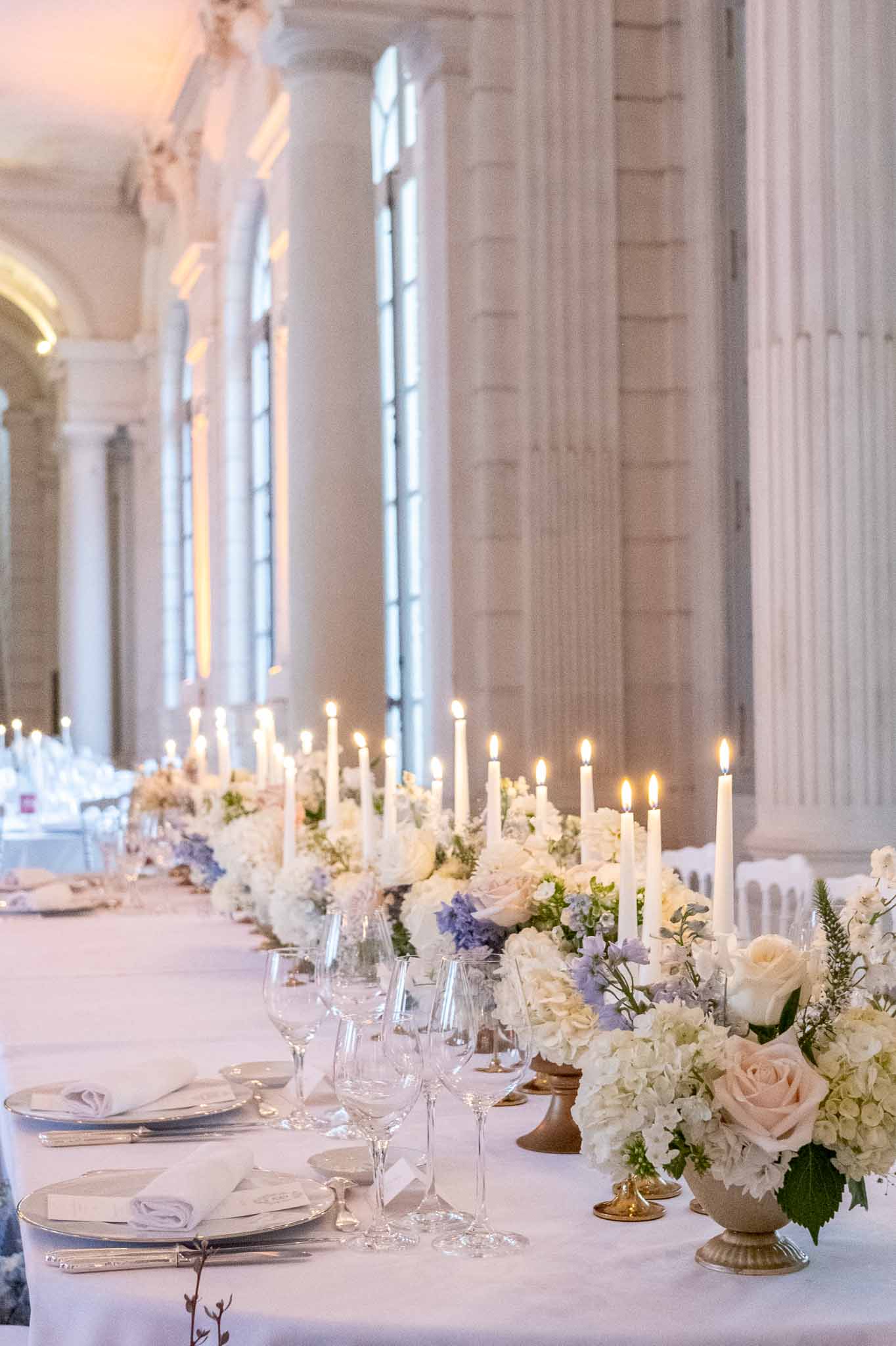 Formal banquet table with ivory linens and floral centerpieces in classical interior with columns