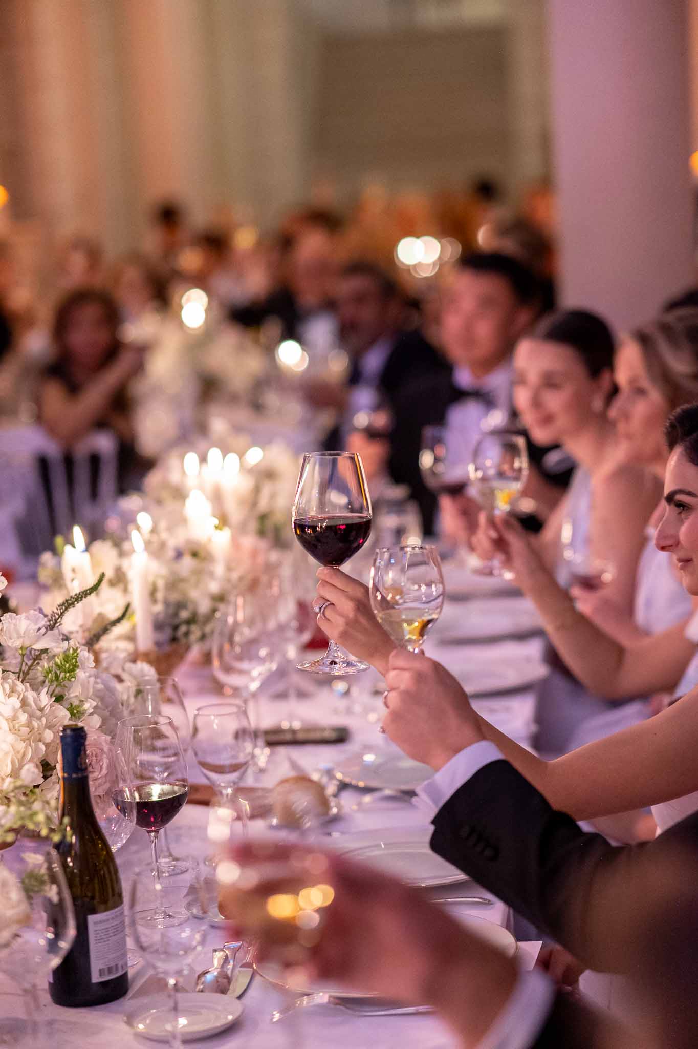 Guest raising wine glass during reception dinner at indoor ballroom with floral centerpieces