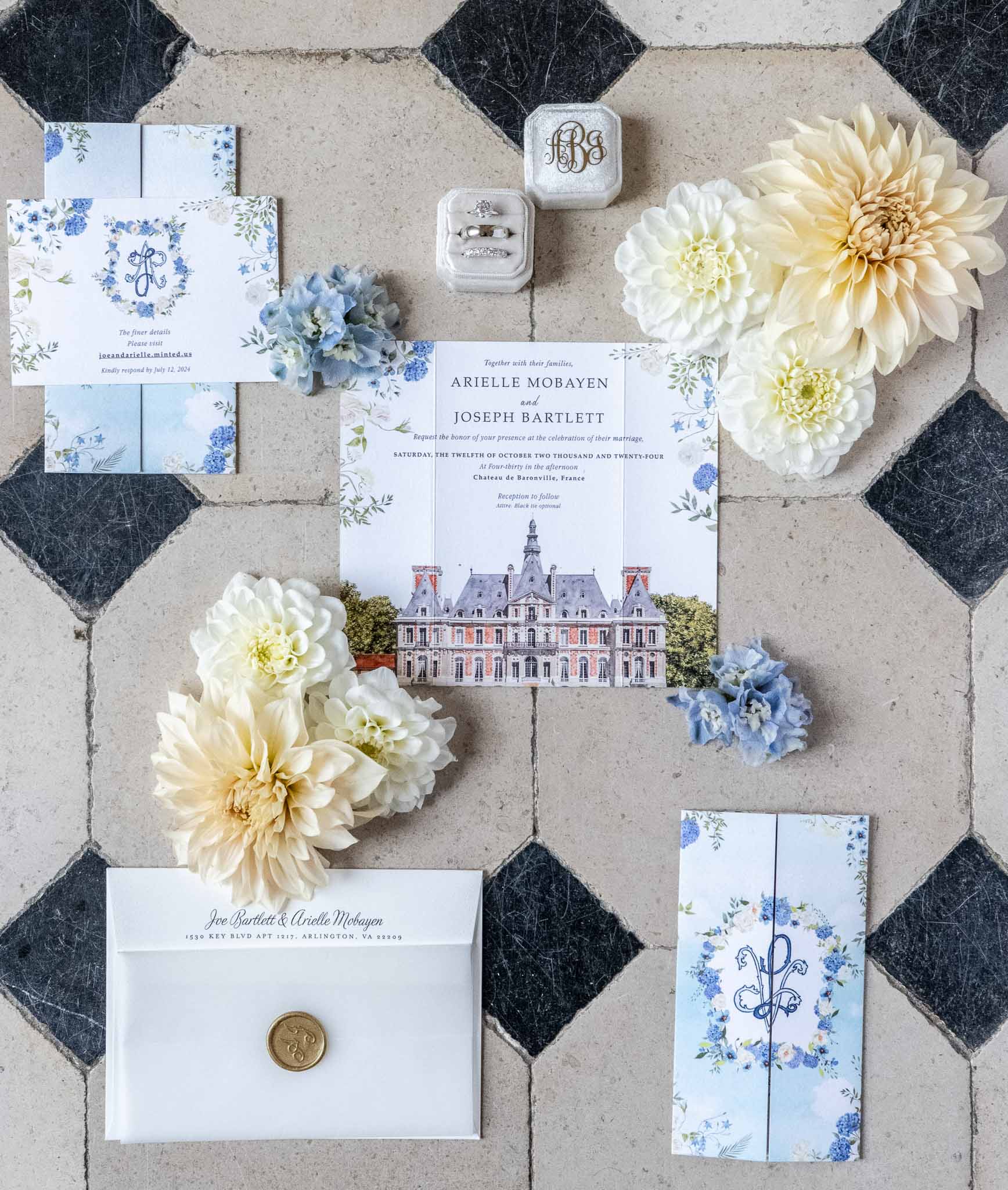 Wedding invitation suite with blue florals and rings arranged on hexagonal tile floor at French château