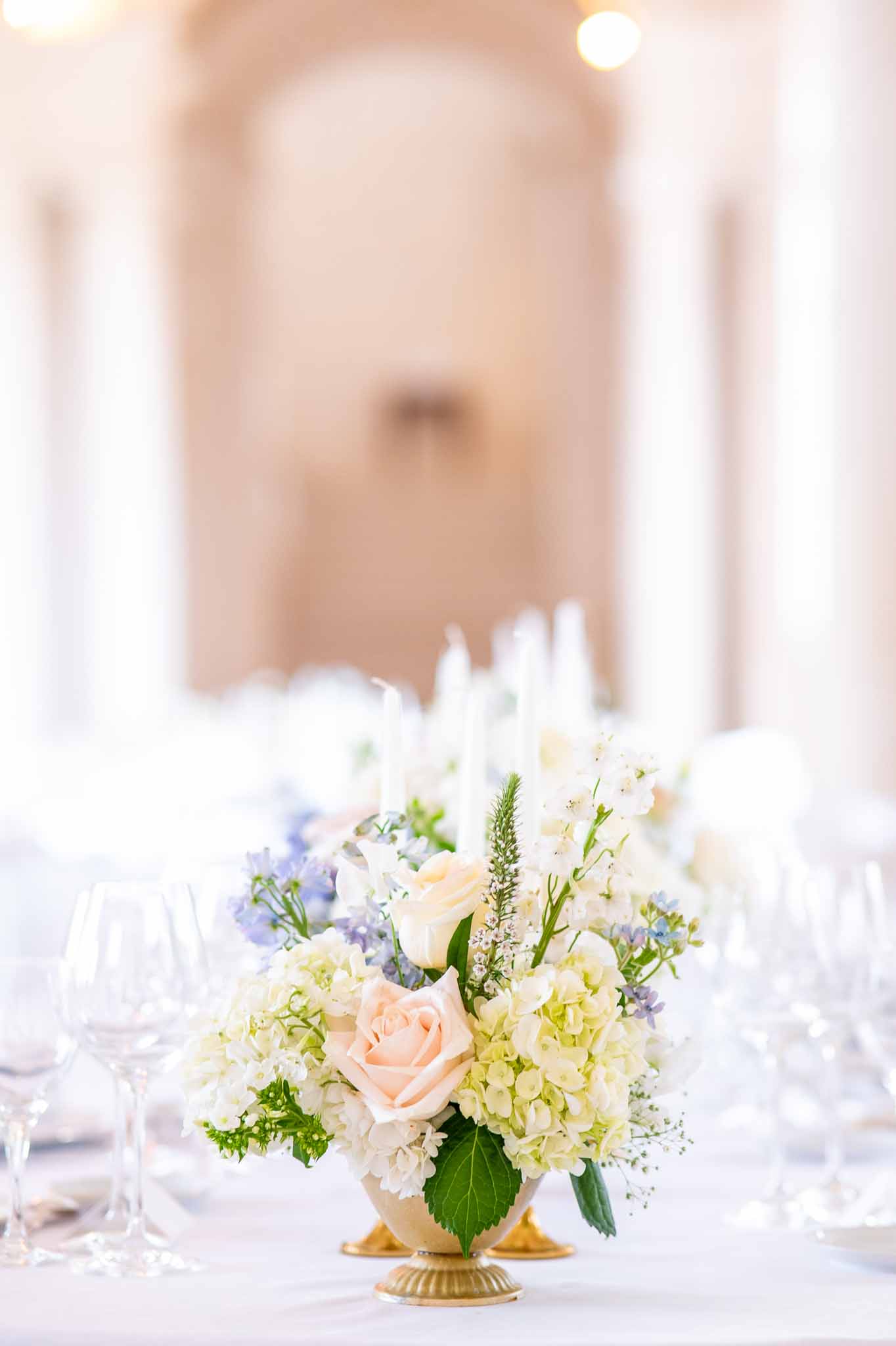 Wedding centerpiece with white hydrangeas and peach roses in champagne urn at indoor reception