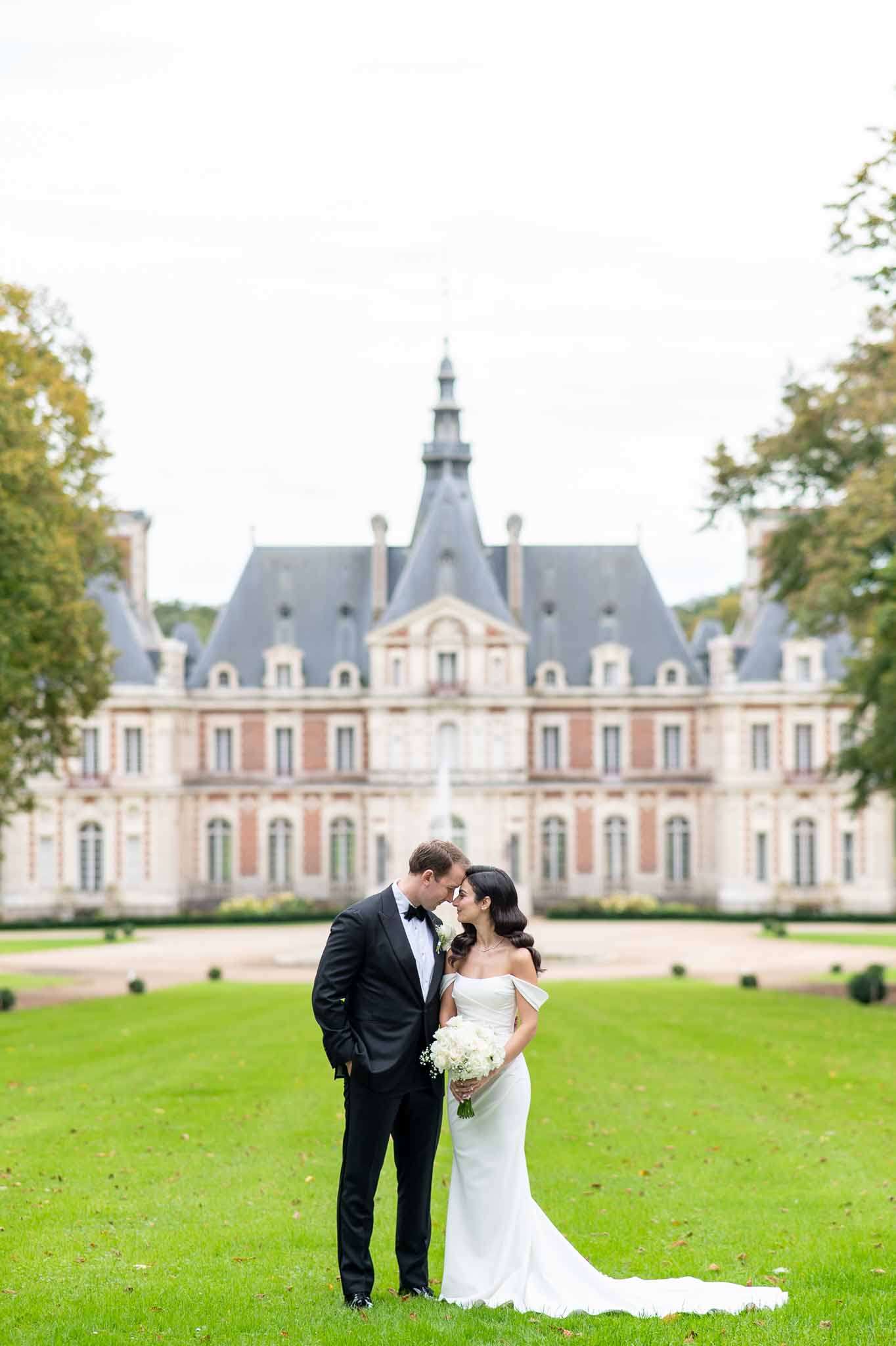 Bride and groom posing together on château lawn during wedding portrait session