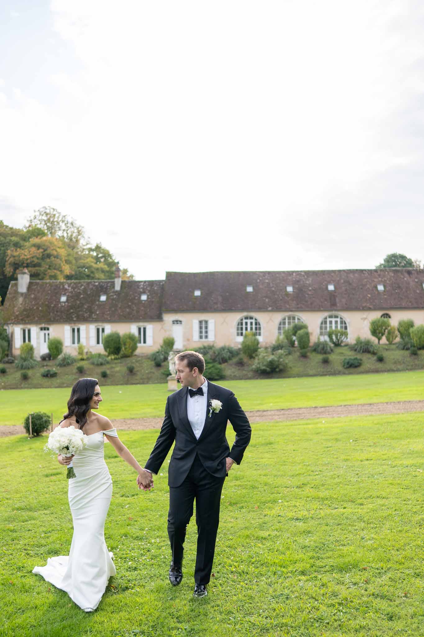 Bride and groom walking hand-in-hand across manicured lawn at stone manor house estate