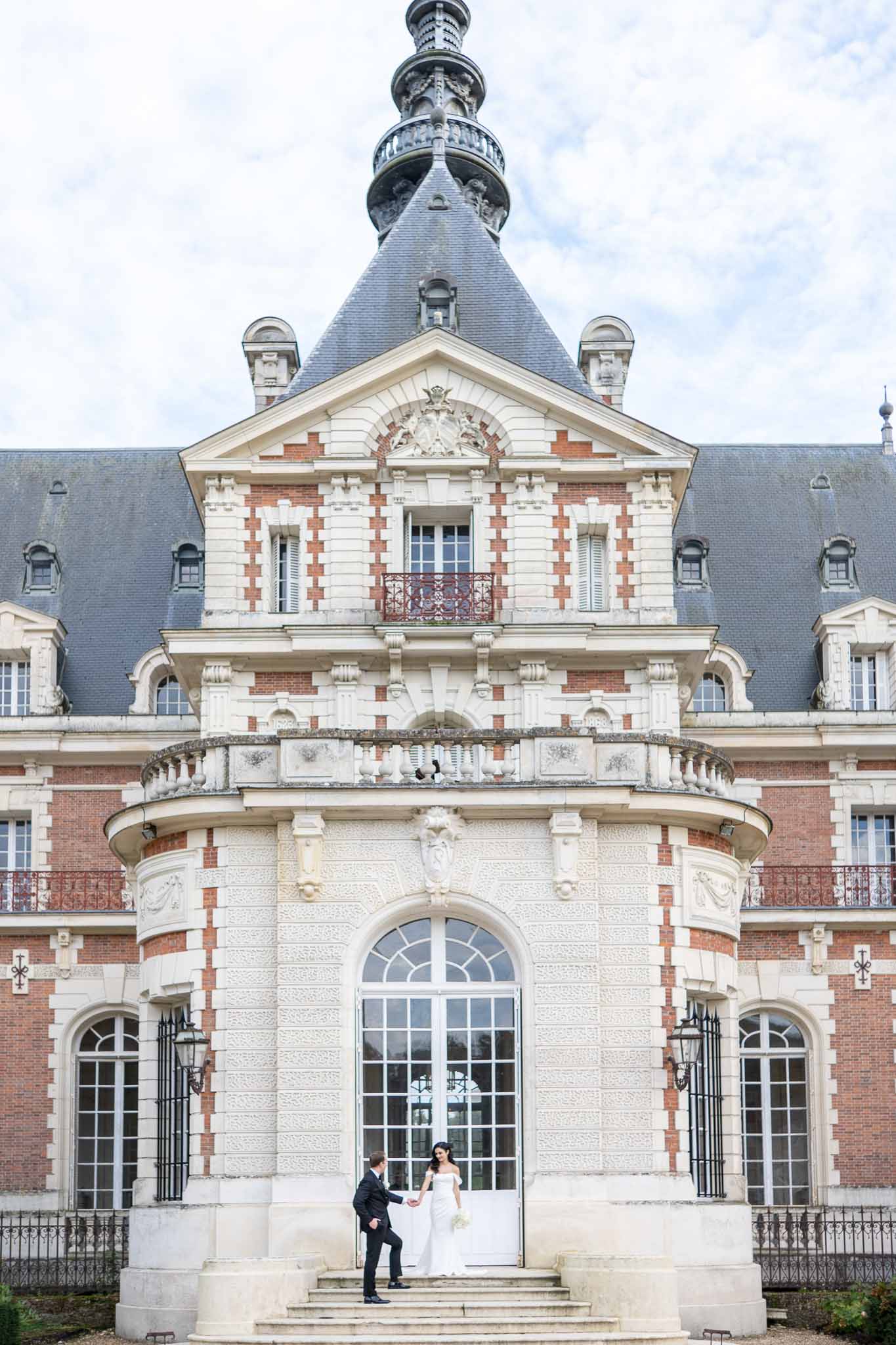 Bride and groom on steps of classical French château with red brick facade and central tower