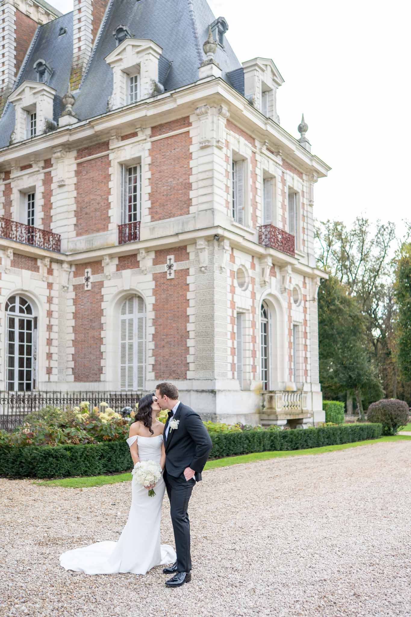 Bride and groom portrait in front of classical French château with mansard roofs and manicured grounds