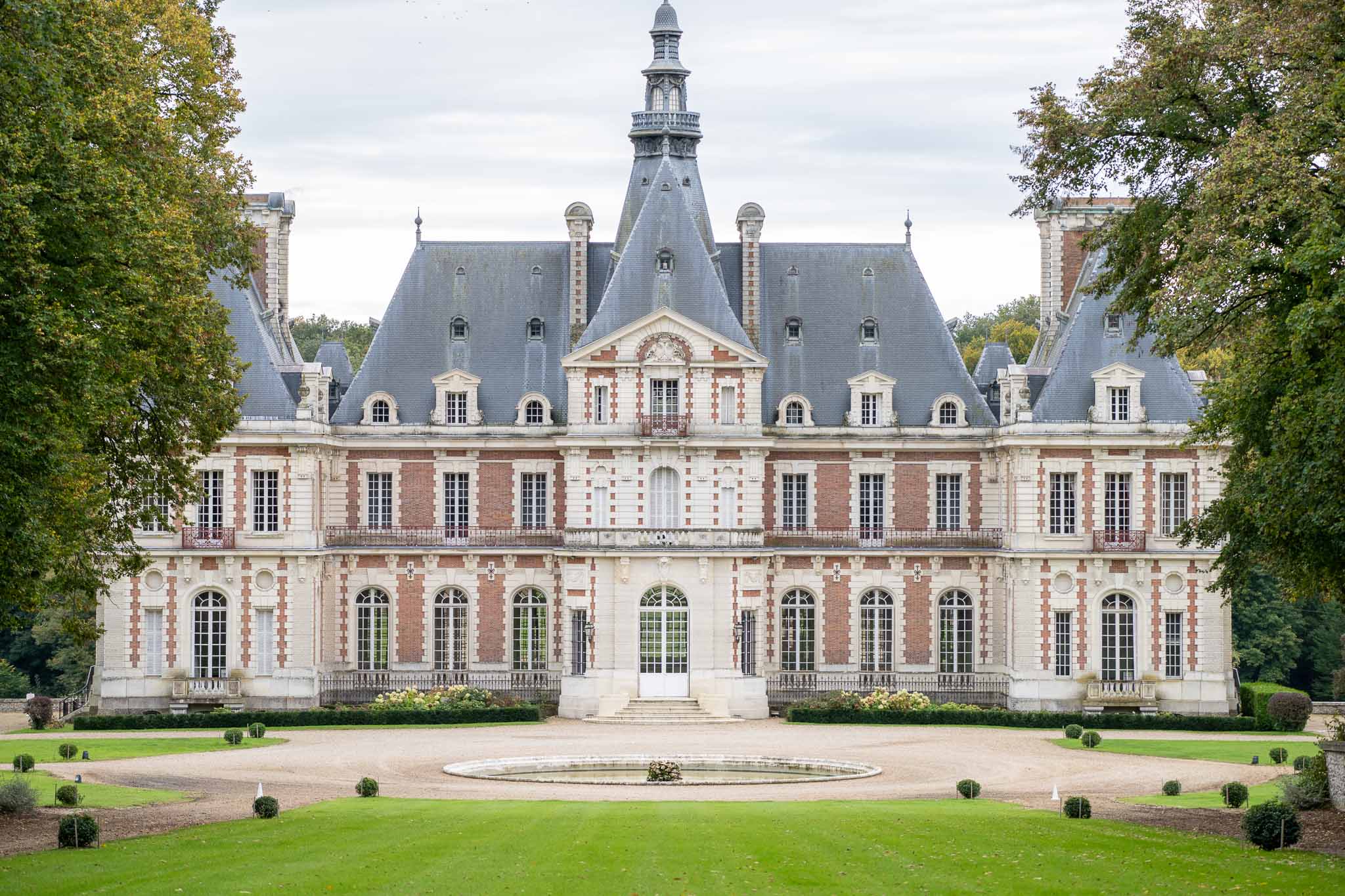 Grand French château with mansard roof and formal courtyard featuring fountain and manicured gardens