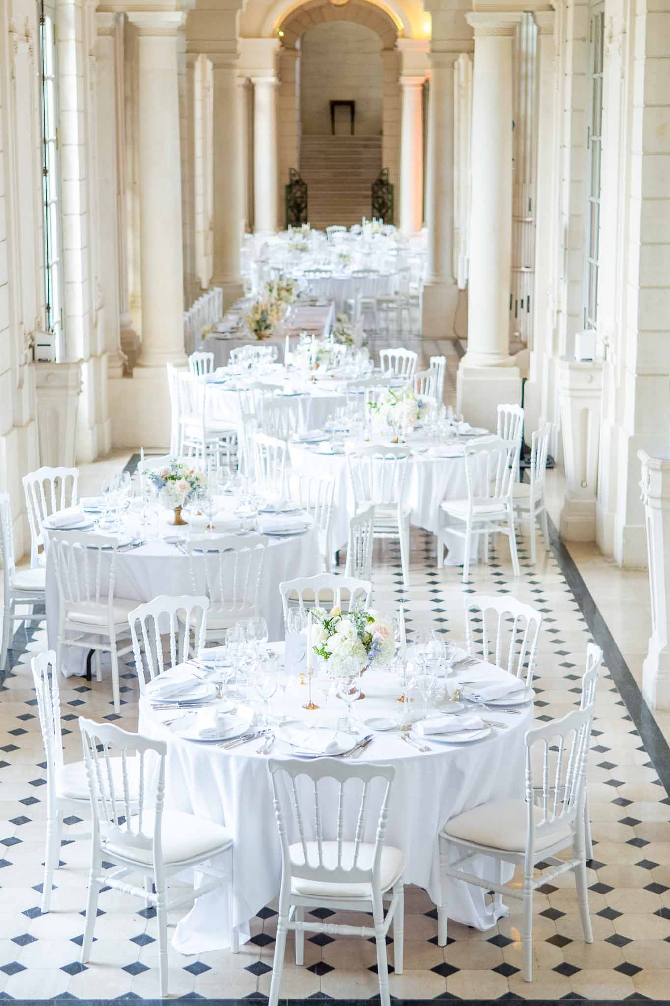 Reception table setup in neoclassical hall with columns and diamond floor pattern