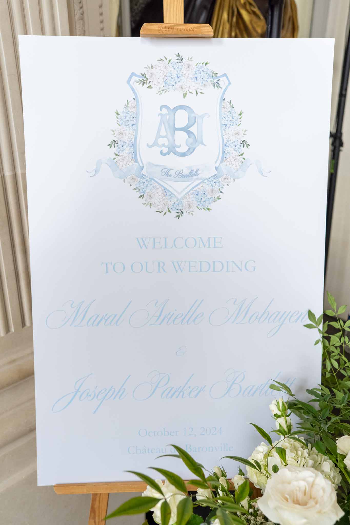 Wedding welcome sign with periwinkle lettering and white roses at indoor venue