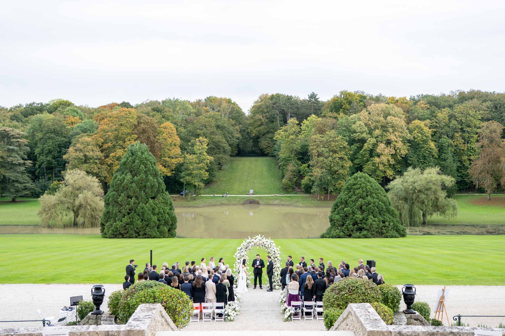 Outdoor wedding ceremony on estate terrace with pond and manicured grounds