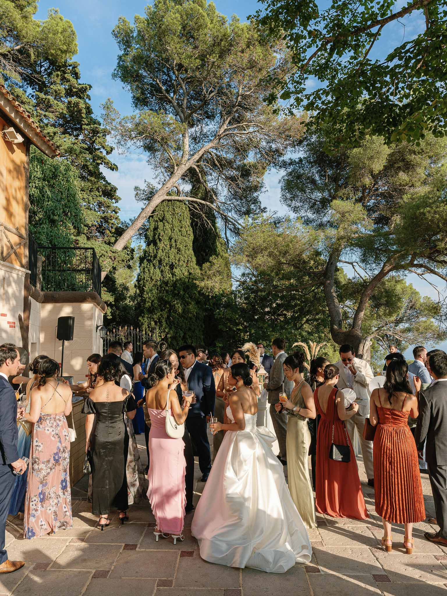 Cocktail hour reception in outdoor courtyard with guests mingling beneath mature trees at Mediterranean villa